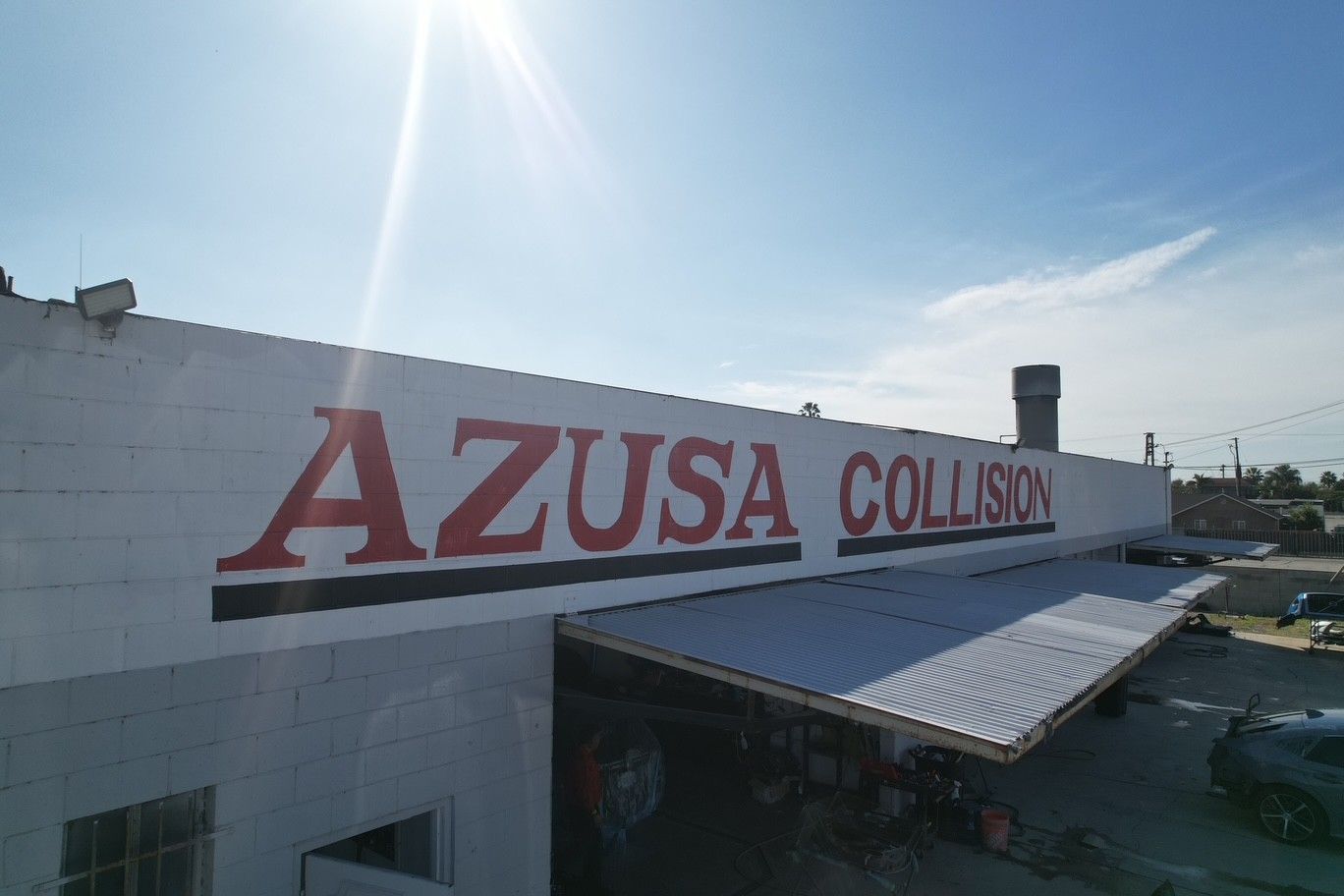 Azusa Collision sign on a white building with a metal awning under bright sunlight