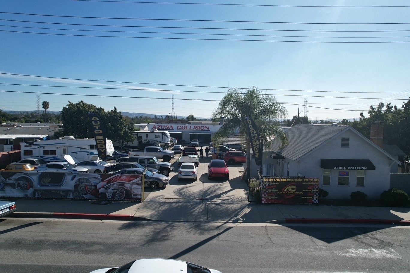Parking lot with many cars, a small white building, and palm trees under a clear sky.