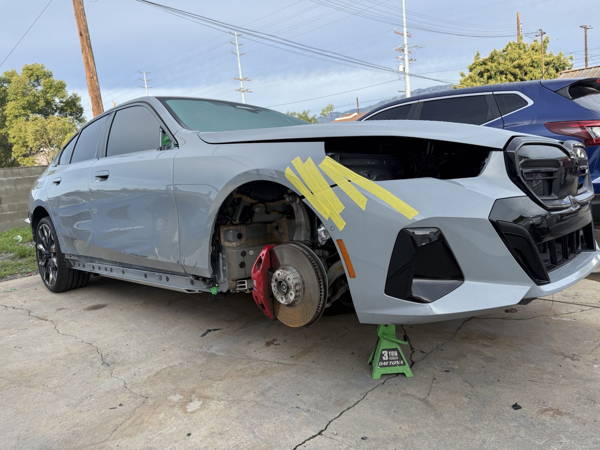 Gray sedan with front-right damage, wheel removed, on jack stands in a repair lot