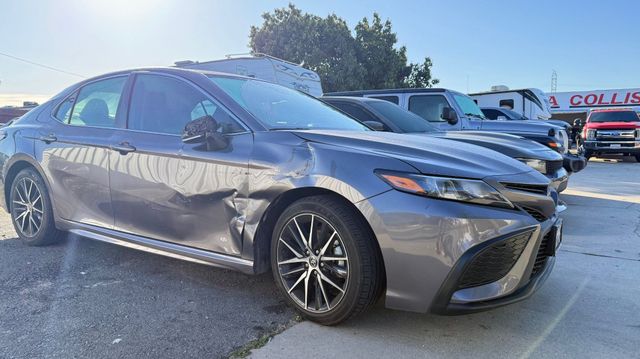 Gray sedan with front-end damage parked in a lot near other vehicles, under bright daylight