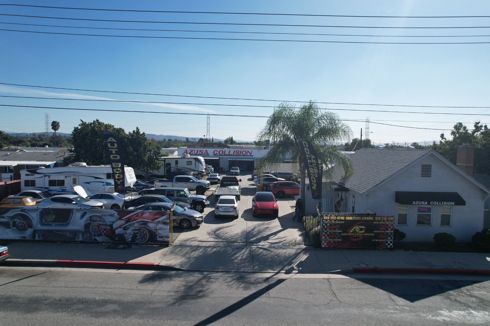 Parking lot with many cars beside a small white building and palm trees under a clear sky
