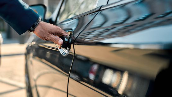 Hand placing a car key into the door lock of a dark car