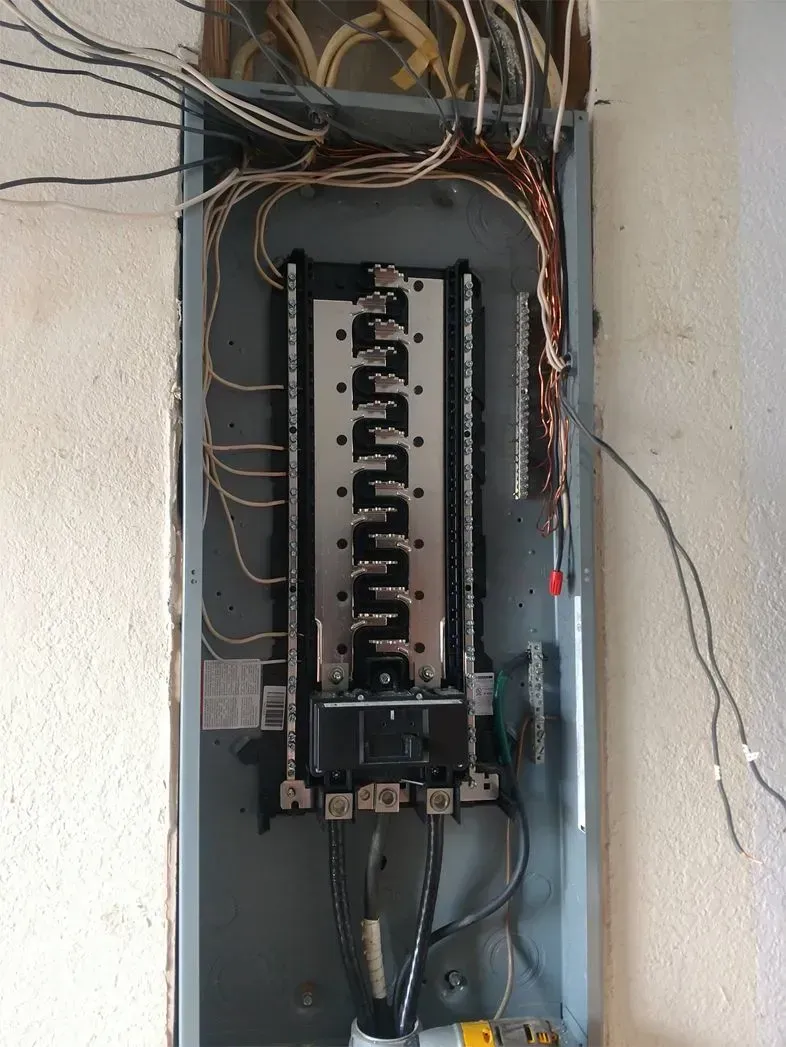 Electrical panel with breakers and wires in a wall cavity.
