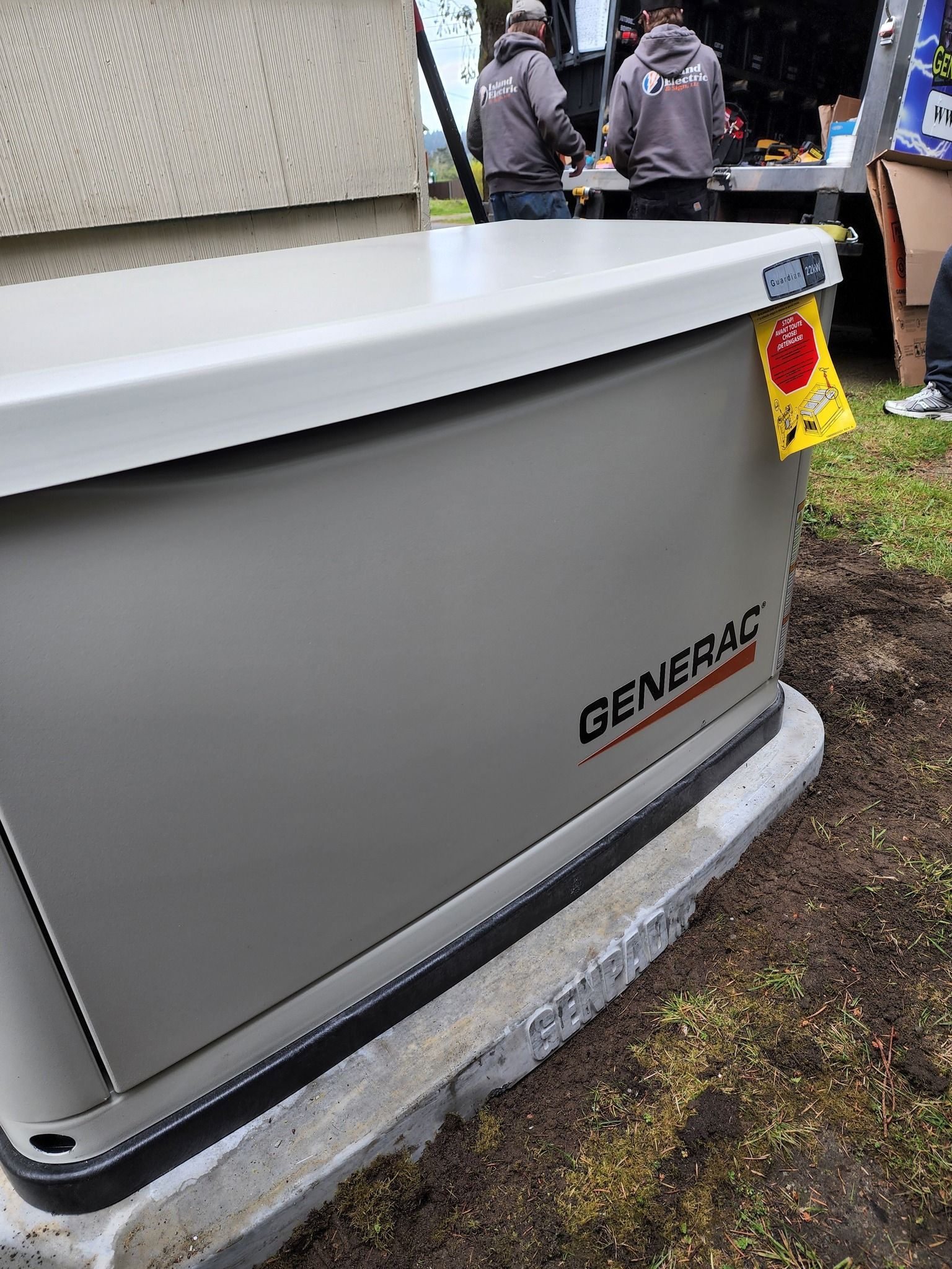 Gray Generac generator installed on concrete base, men in background.