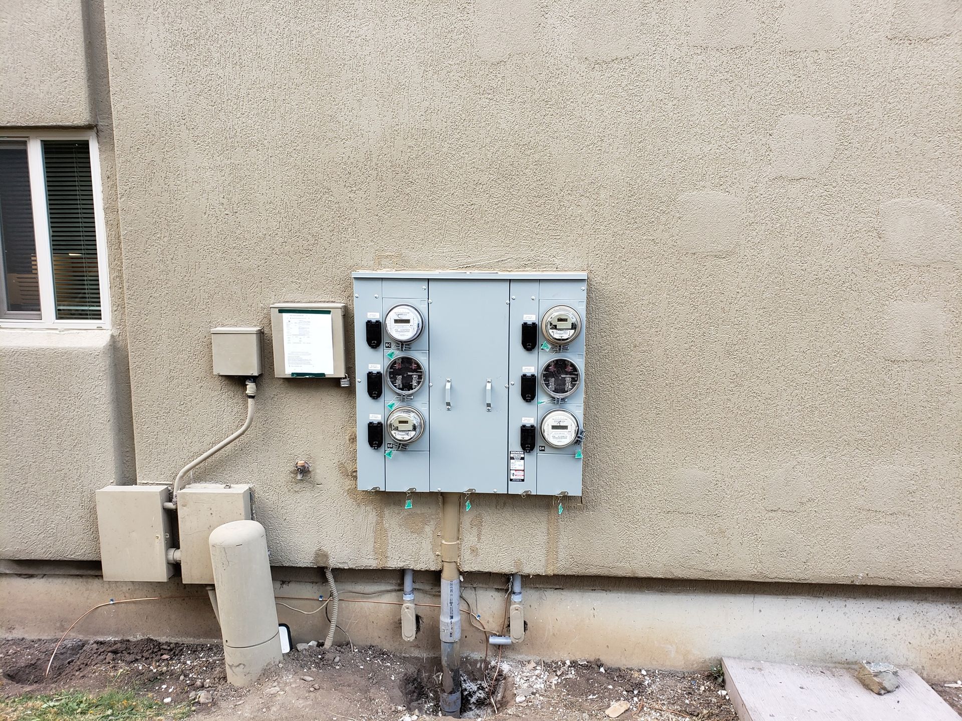 Gray electrical meter panel on a textured building exterior.