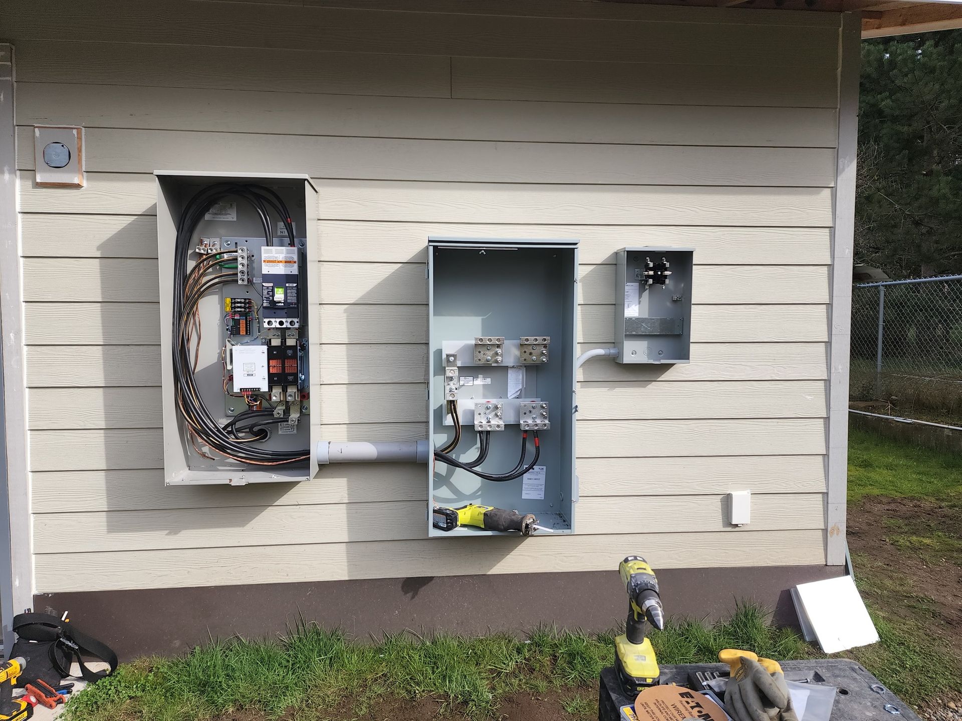 Electrical boxes mounted on a beige building exterior with exposed wiring and a partially open box.