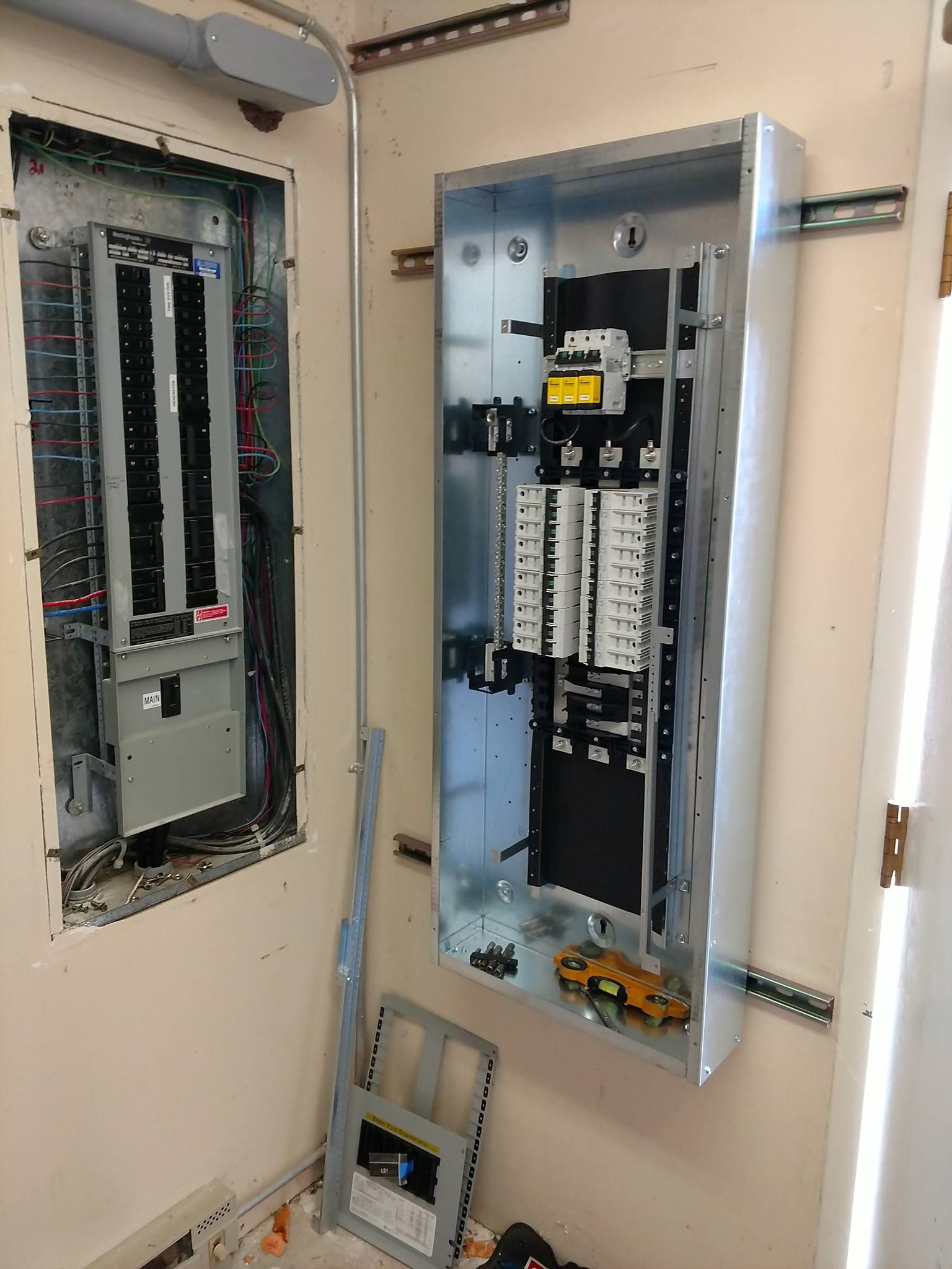 Two electrical panels mounted on a beige wall, with conduit and tools.