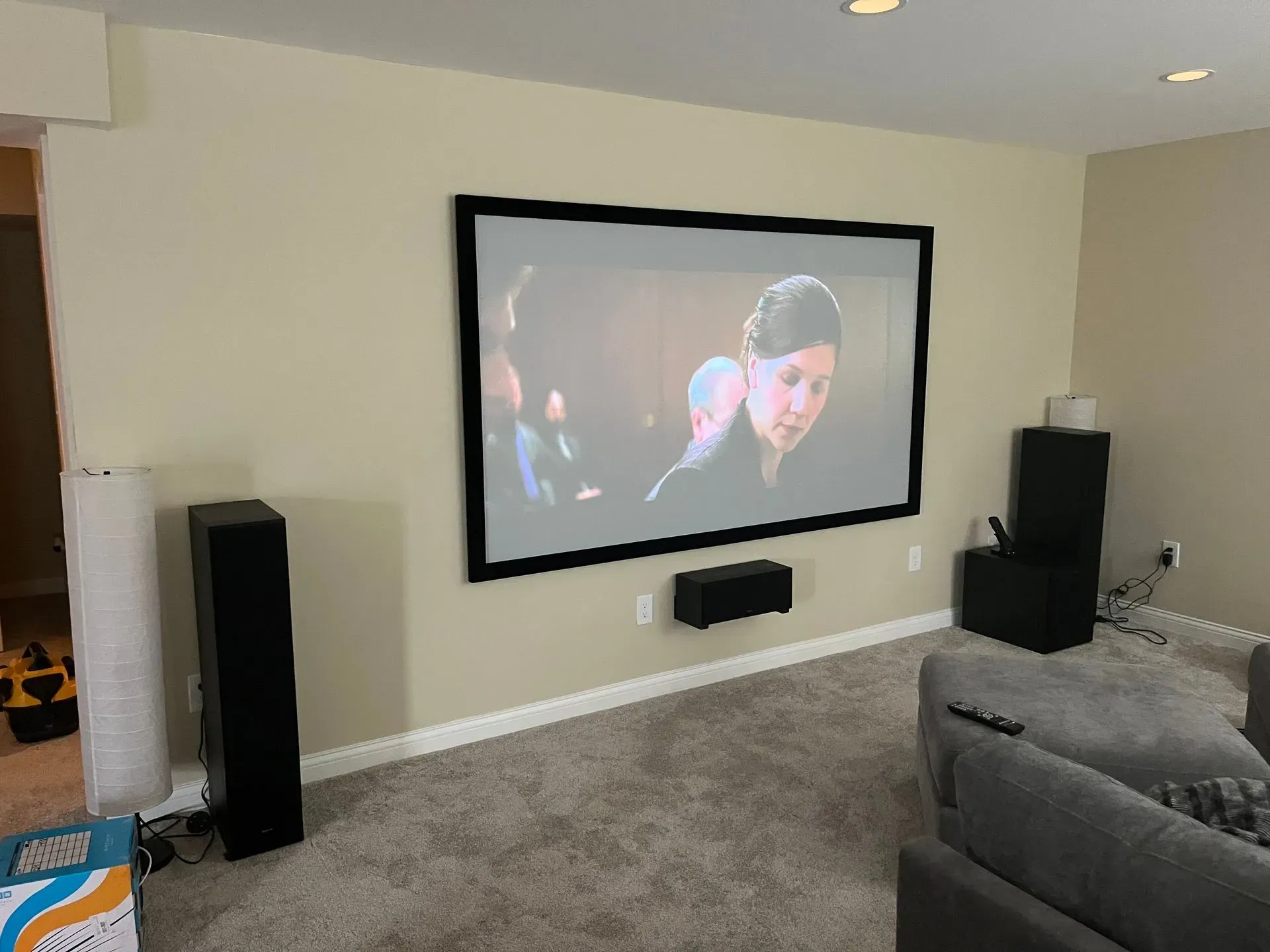 A home theater setup with a wall-mounted projection screen, center channel speaker, and floor-standing speakers.