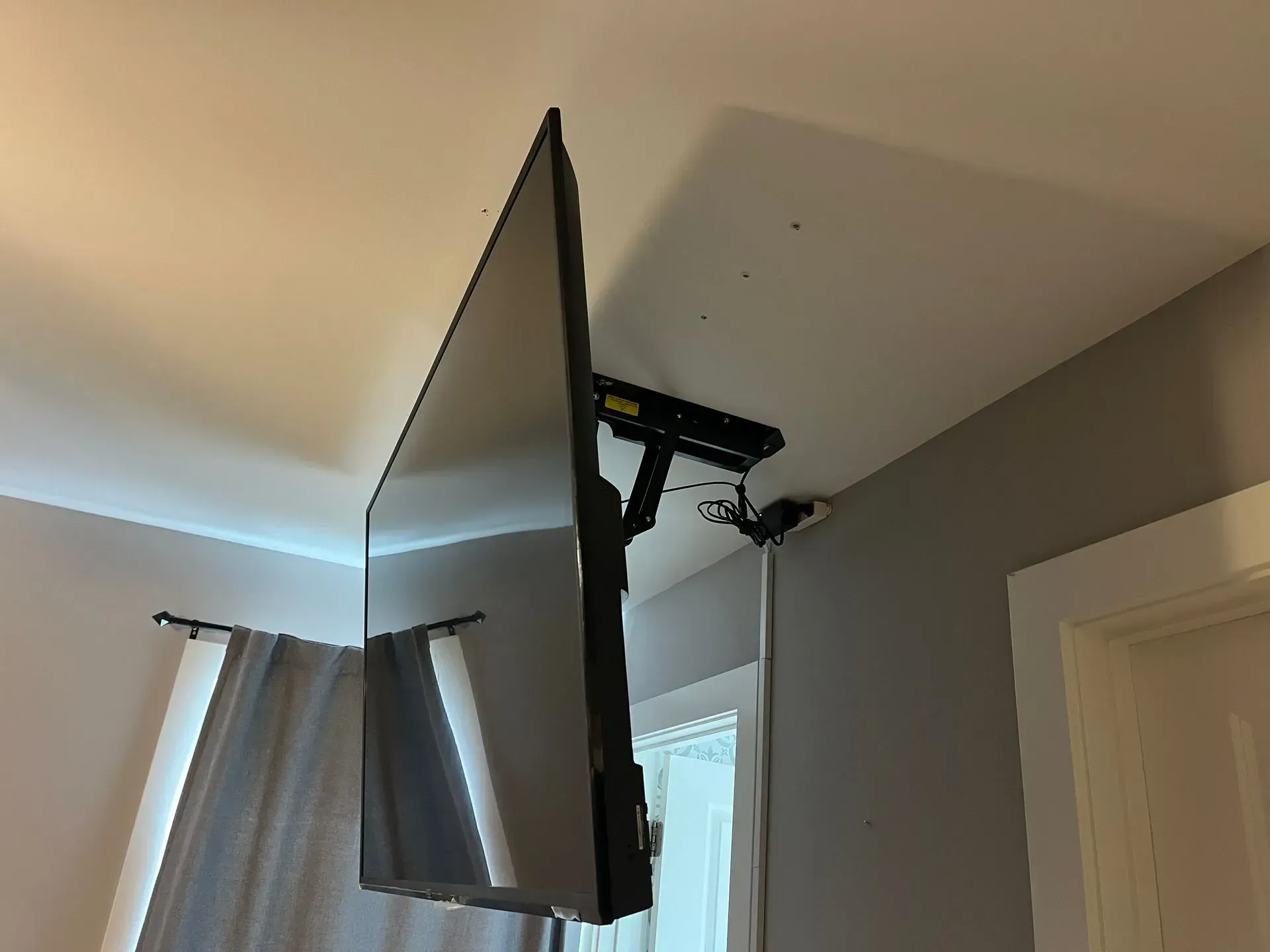 A black television mounted to a white ceiling with an adjustable black metal bracket in a room.