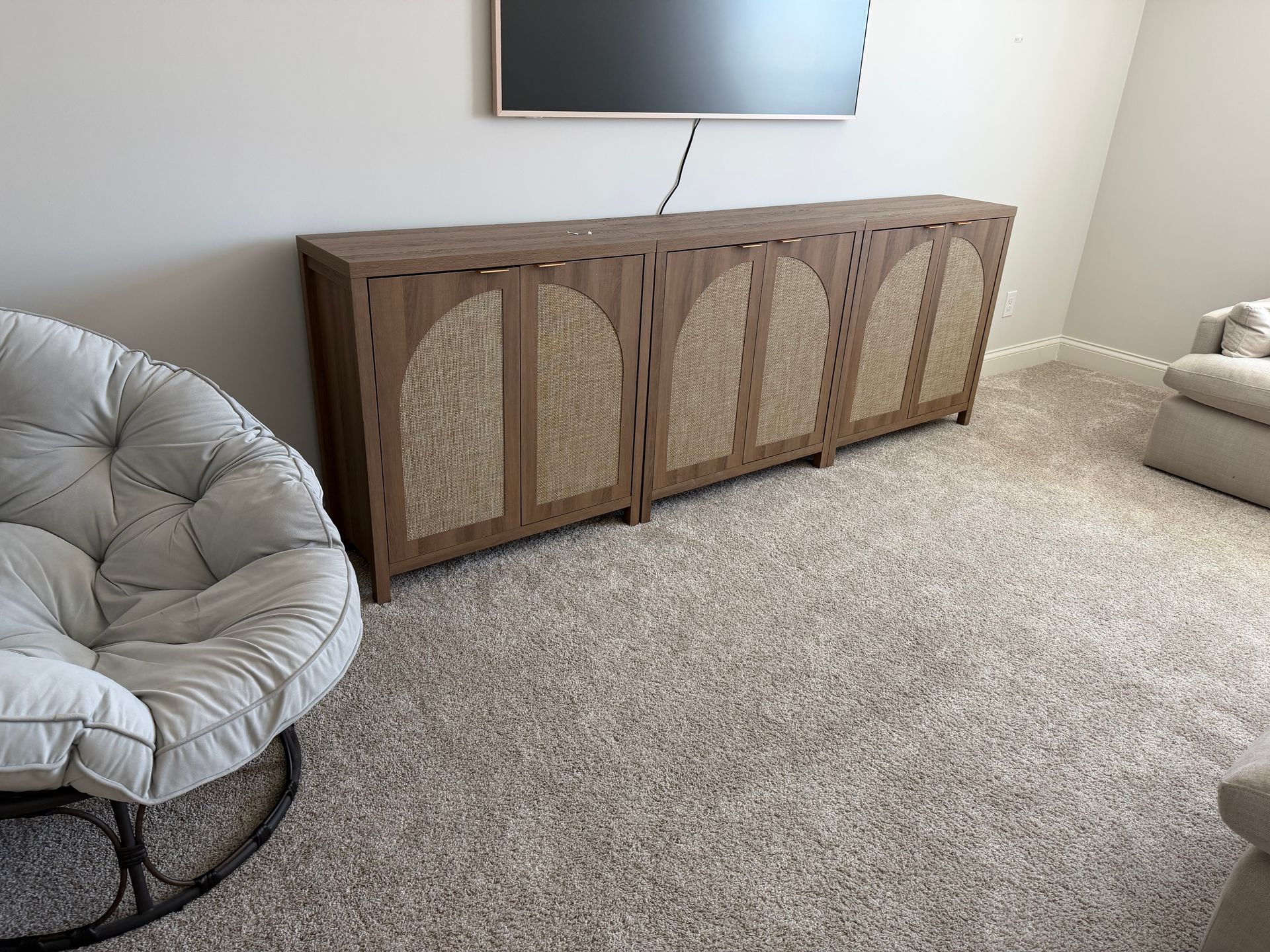 A long, brown wooden media console with arched, woven cane door panels sits against a wall below a mounted television.