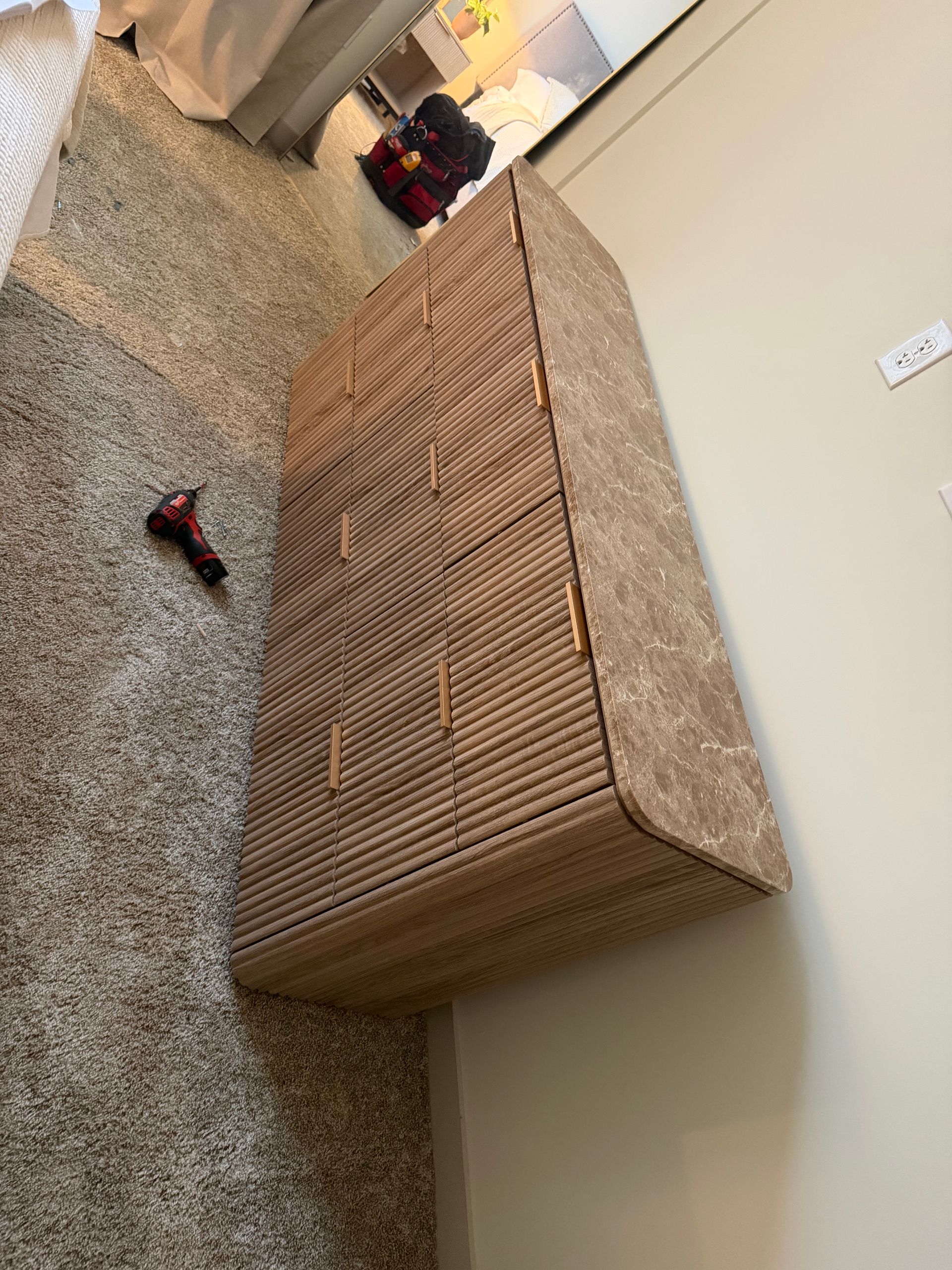 A tall, six-drawer dresser with a textured, light brown finish sits on a carpeted floor against a wall.