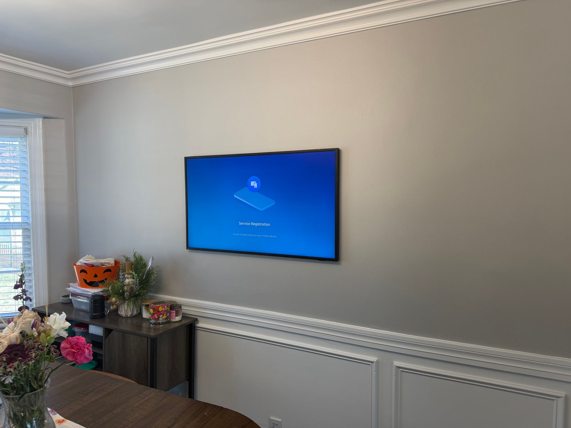 A mounted television displays a blue screen with a connection icon on a light gray wall above wainscoting.