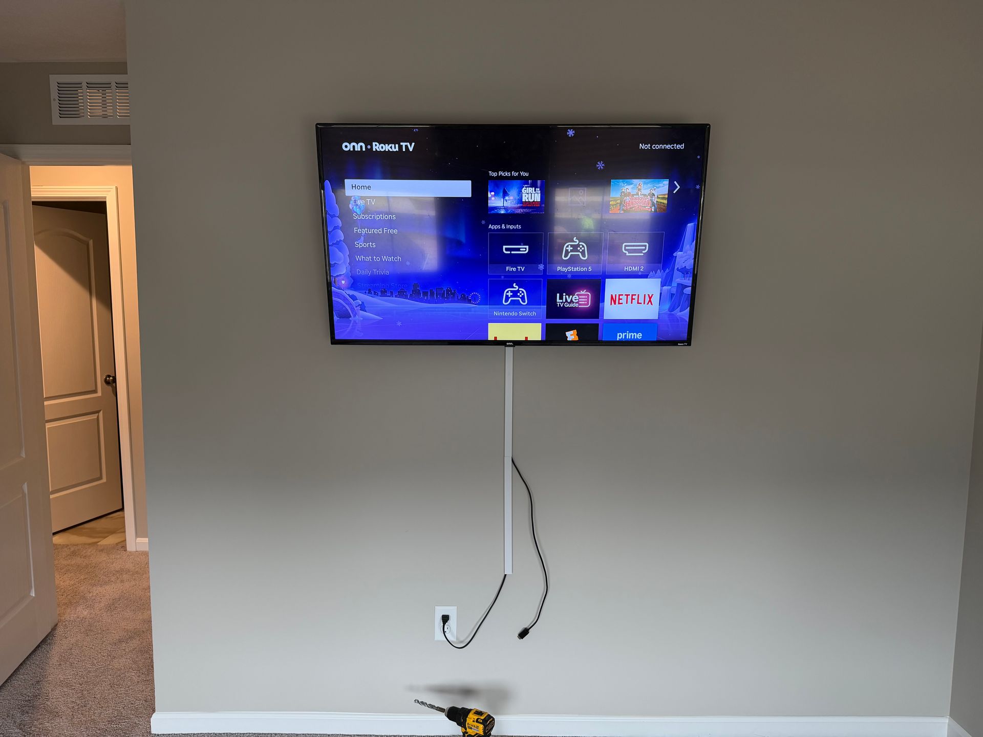 A wall-mounted TV showing a menu screen with exposed cables running down the wall into a white cable management cover.