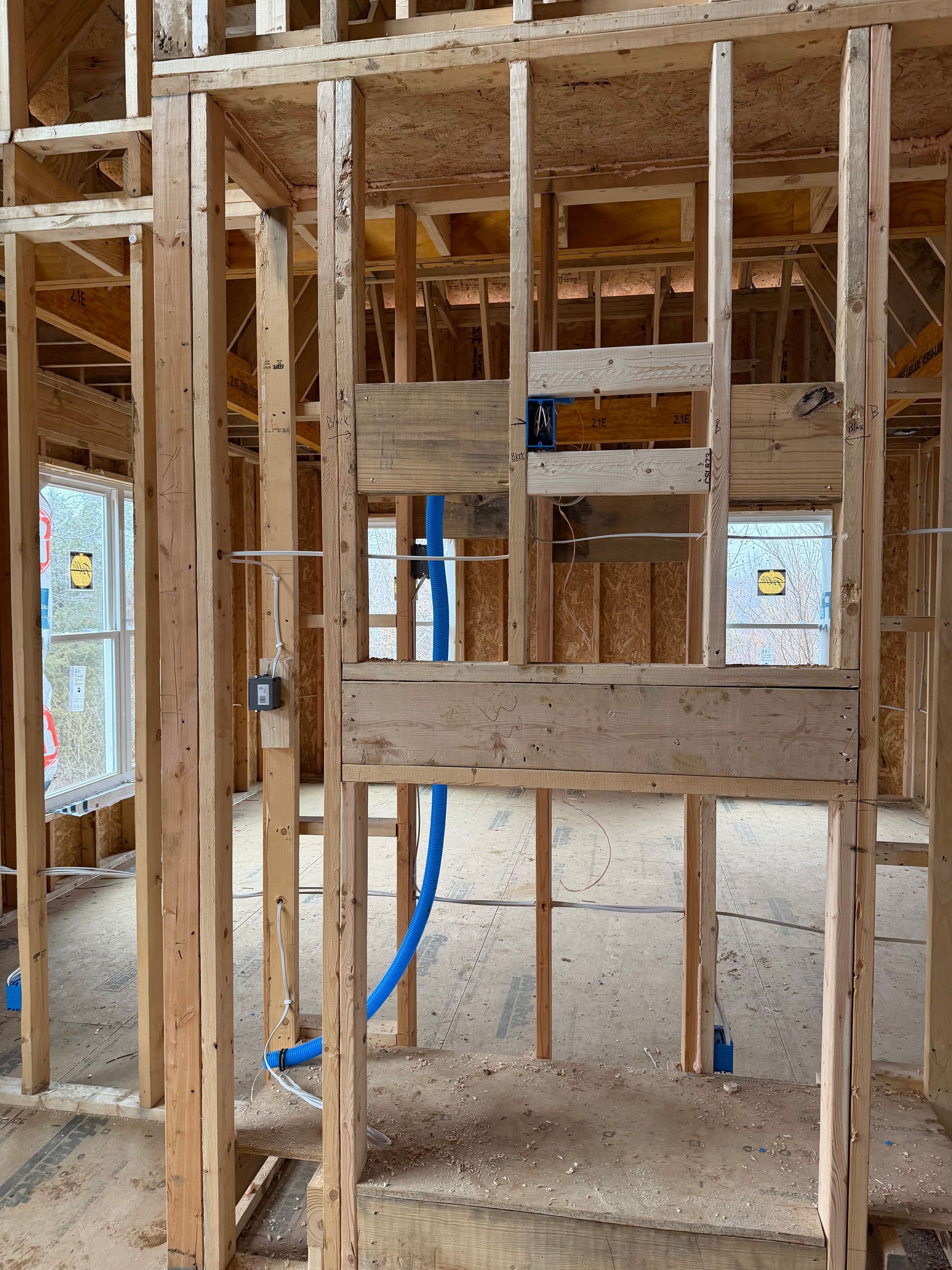 The interior wood framing of a new house construction, featuring exposed studs and blue electrical conduits.