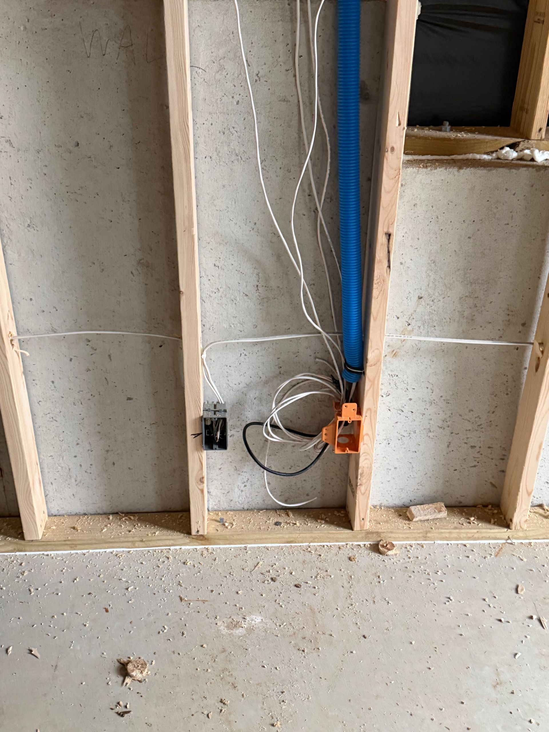 Rough-in electrical wiring and a plastic utility box mounted on wooden wall studs against a concrete foundation wall.