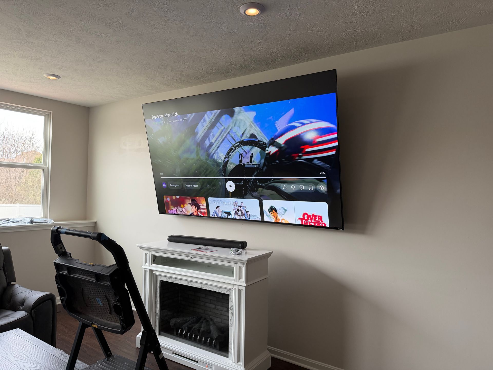 A wall-mounted television displays a video above a white electric fireplace in a living room.