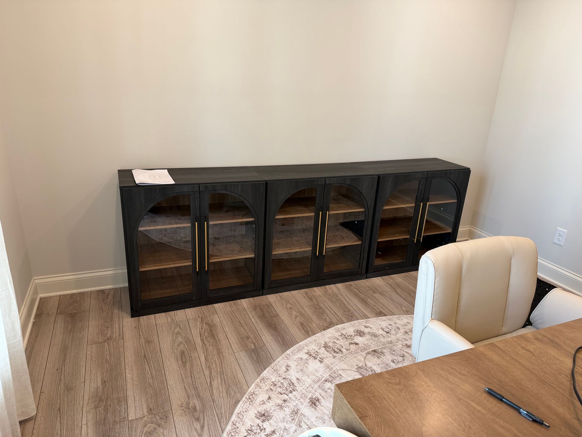 A low, black, three-section cabinet with arched glass doors and gold hardware sits against a wall in a room.