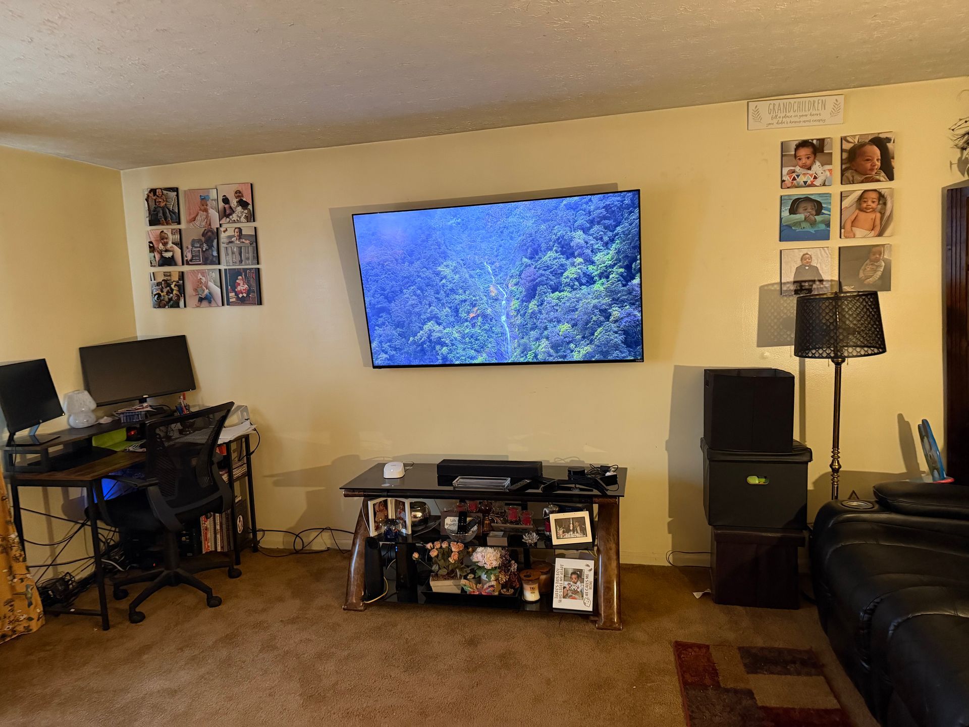 A living room featuring a wall-mounted television, a computer desk in the corner, a media console, and wall decorations.