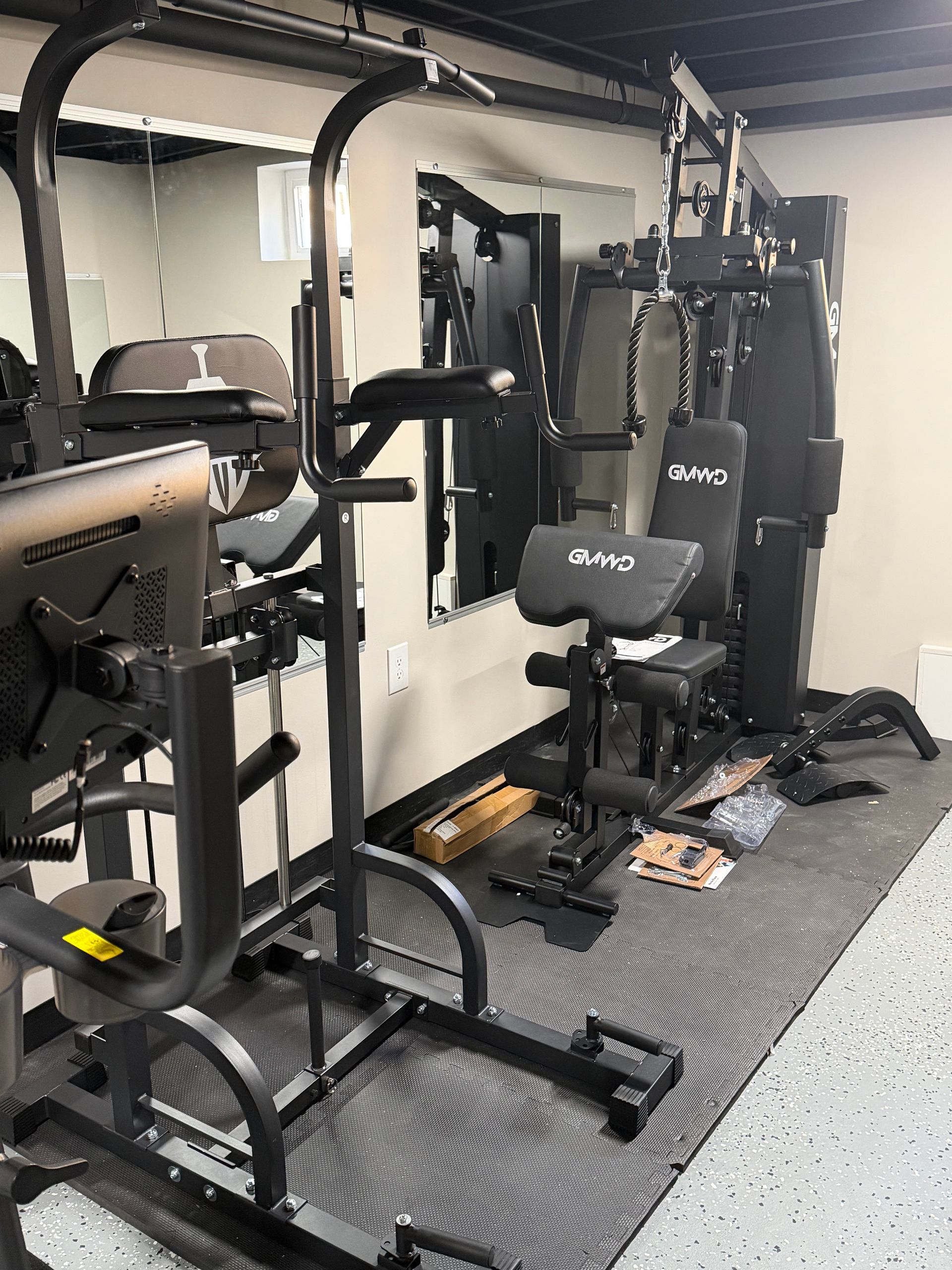 A home gym area featuring a pull-up station in the foreground and a multi-station weight machine in the background.