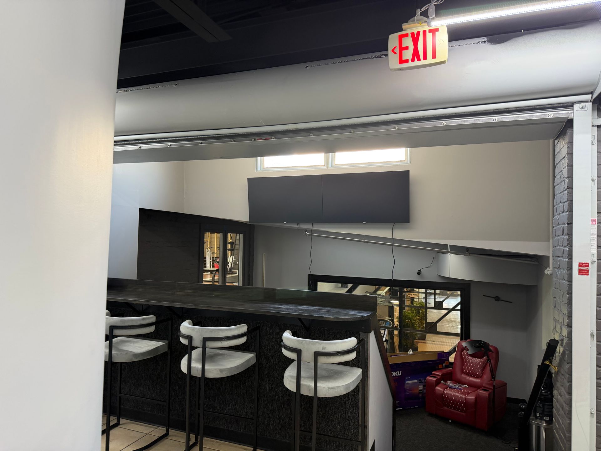 A raised counter with three white bar stools overlooks an indoor space featuring a red chair and a black accent wall.