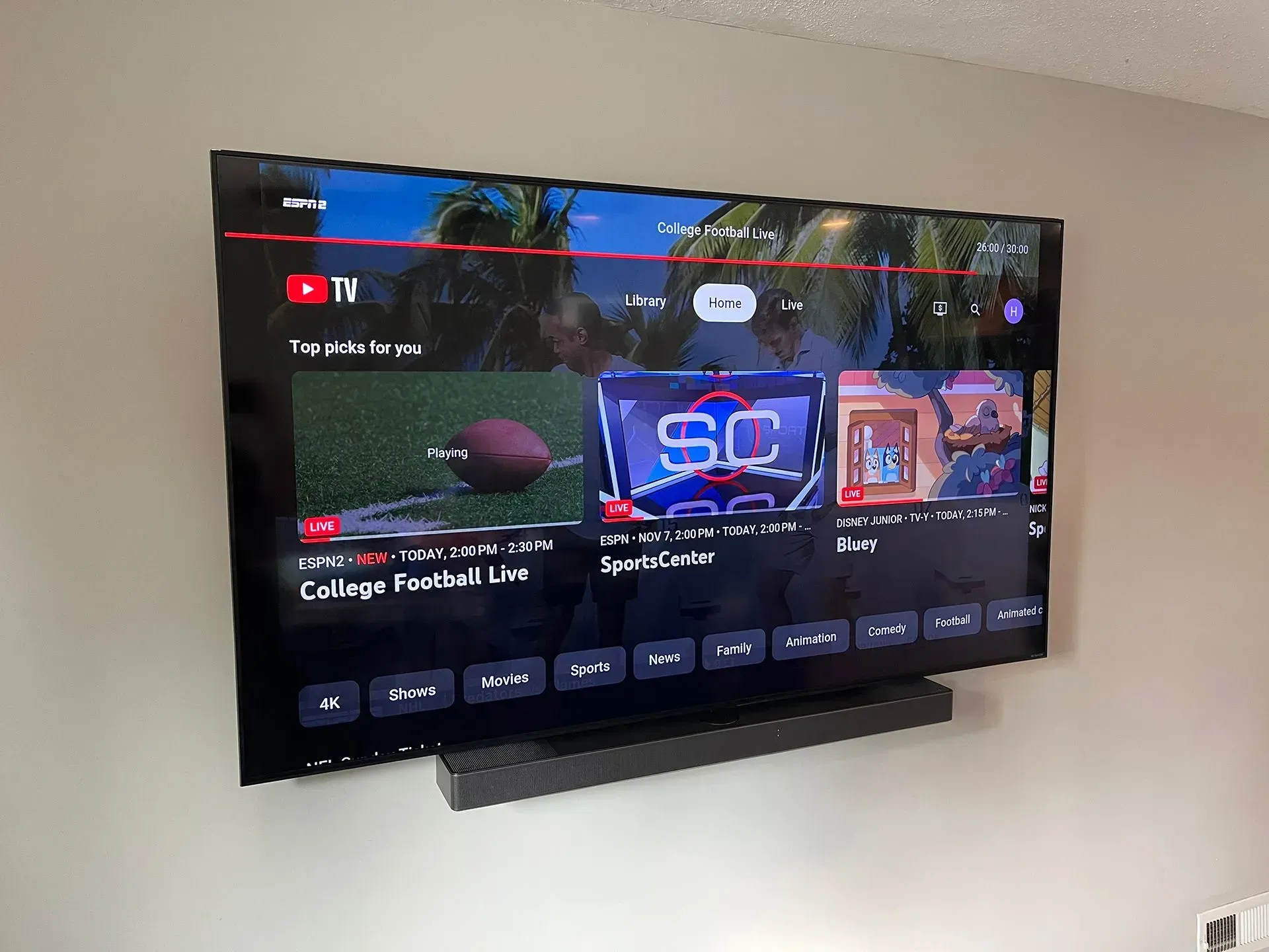 A wall-mounted flat-screen television displays the YouTube TV home screen above a dark horizontal soundbar.