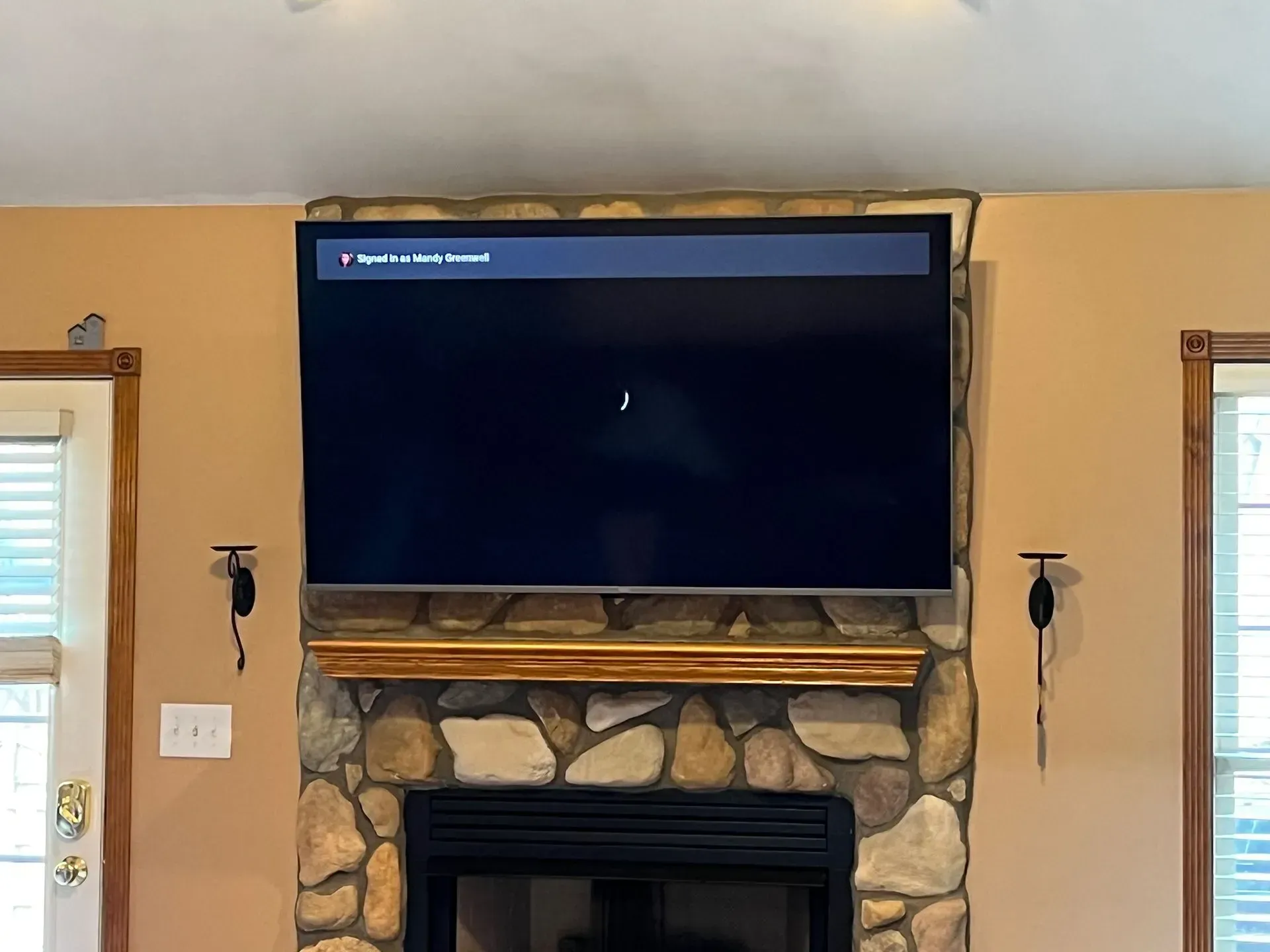 A flat-screen television mounted above a stone fireplace, displaying a dark loading screen with a small musical note icon.