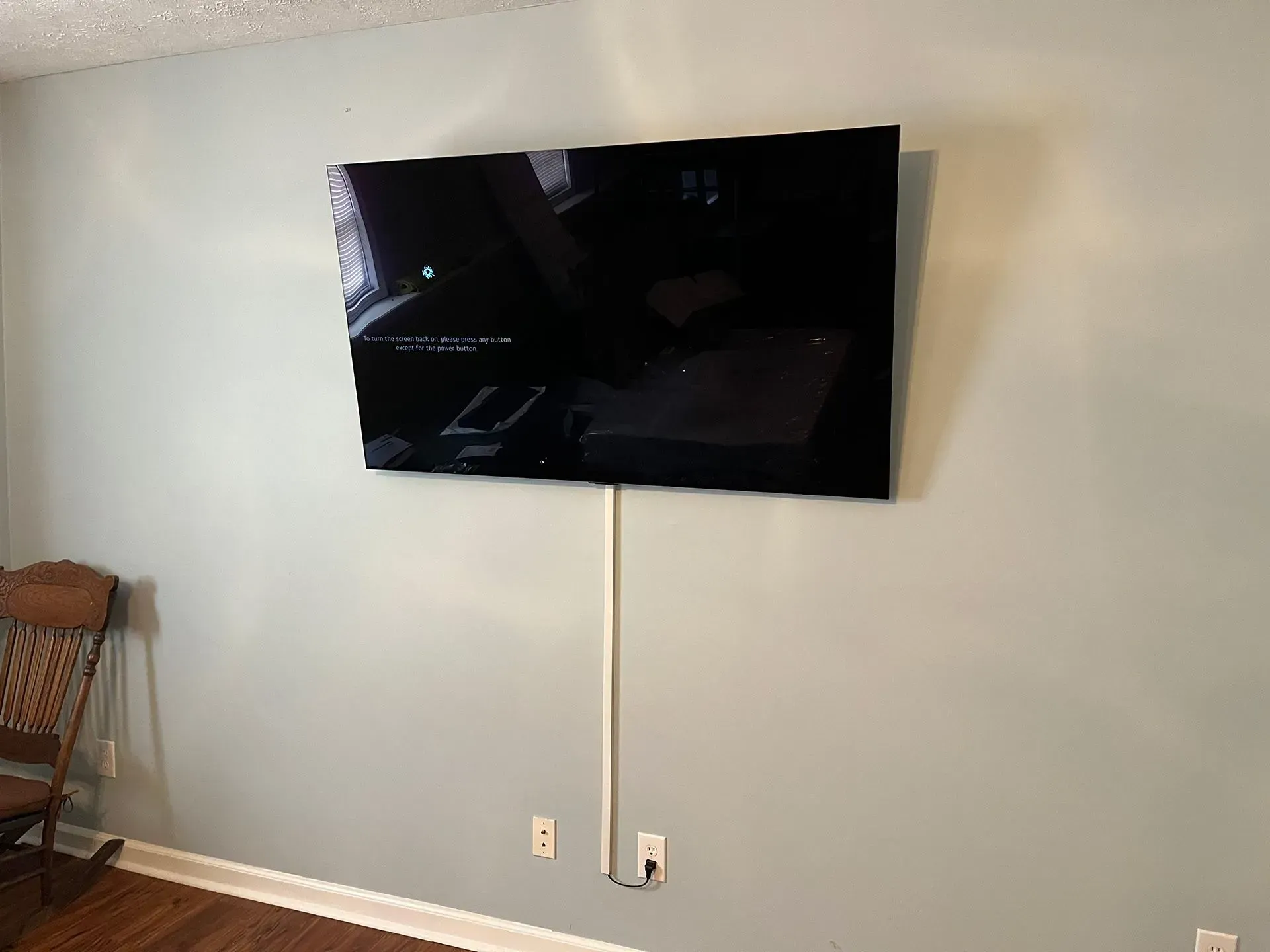 A television mounted on a light blue wall with a white cable cover running down to an electrical outlet.