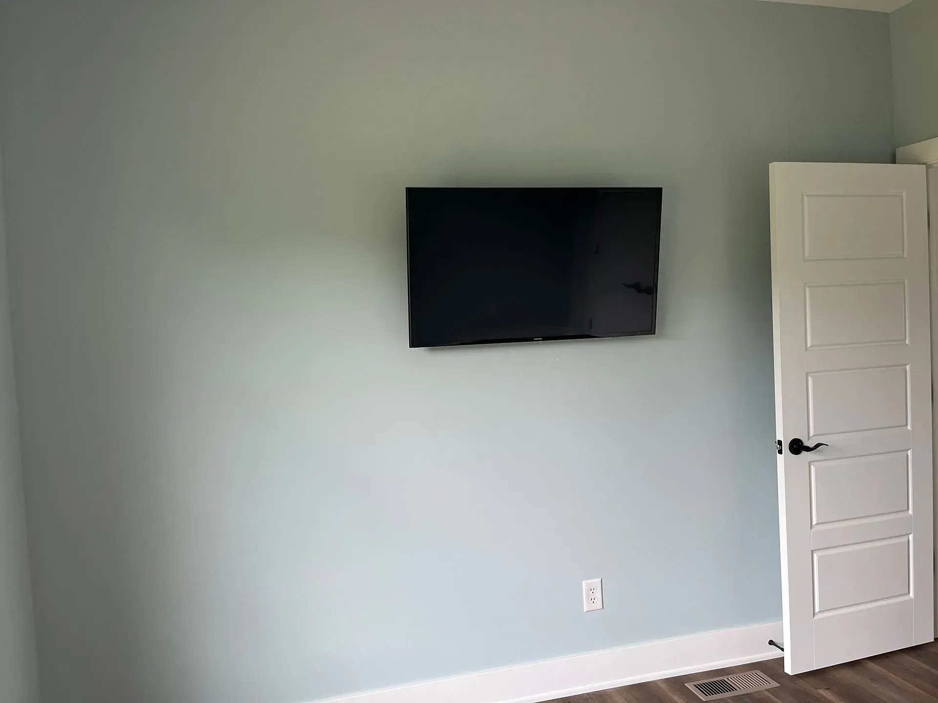 A black television mounted on a light blue wall, adjacent to a white interior door.