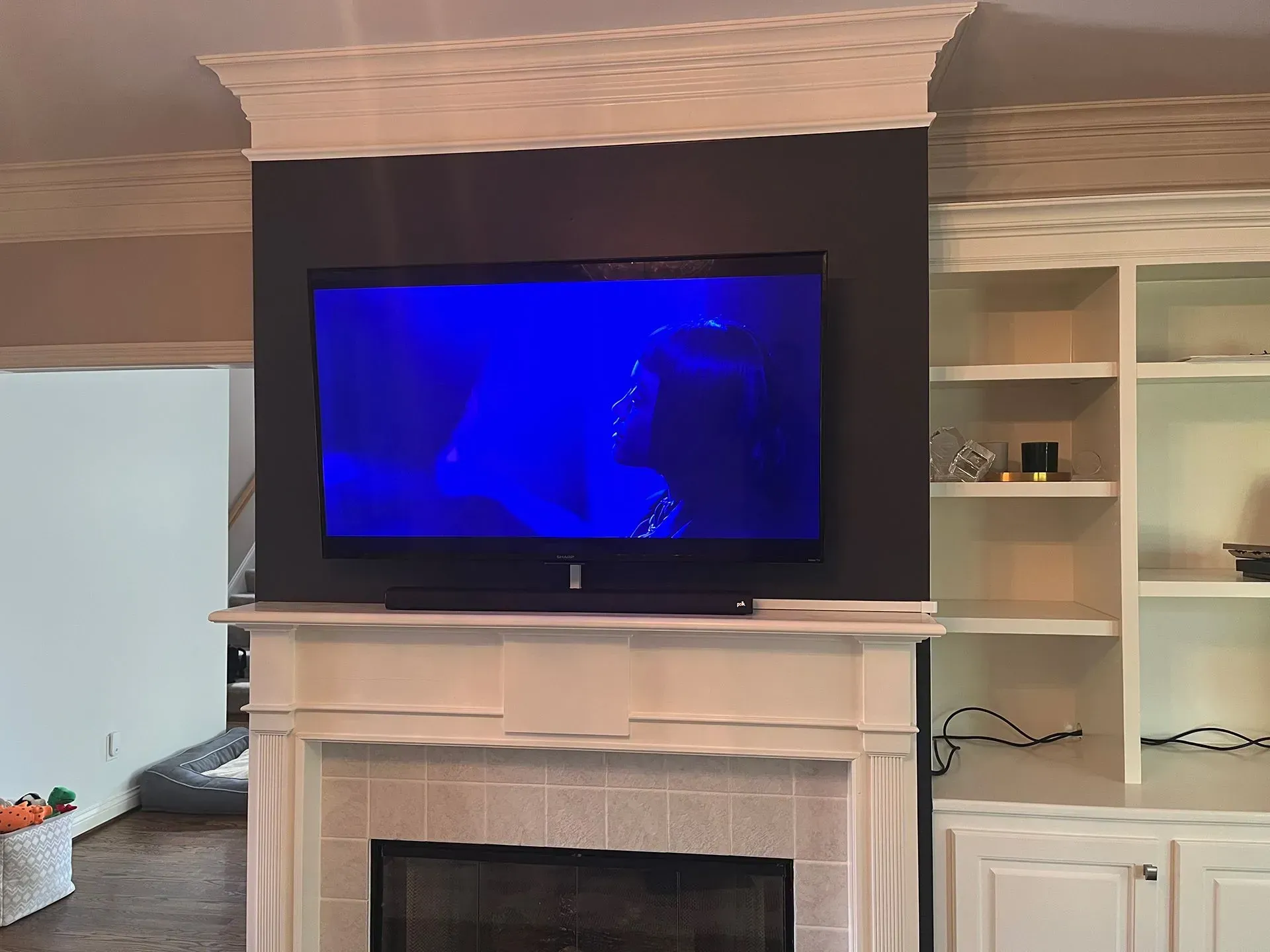 A flat-screen TV displaying a blue-tinted scene, mounted above a white fireplace mantel and shelves in a living room.