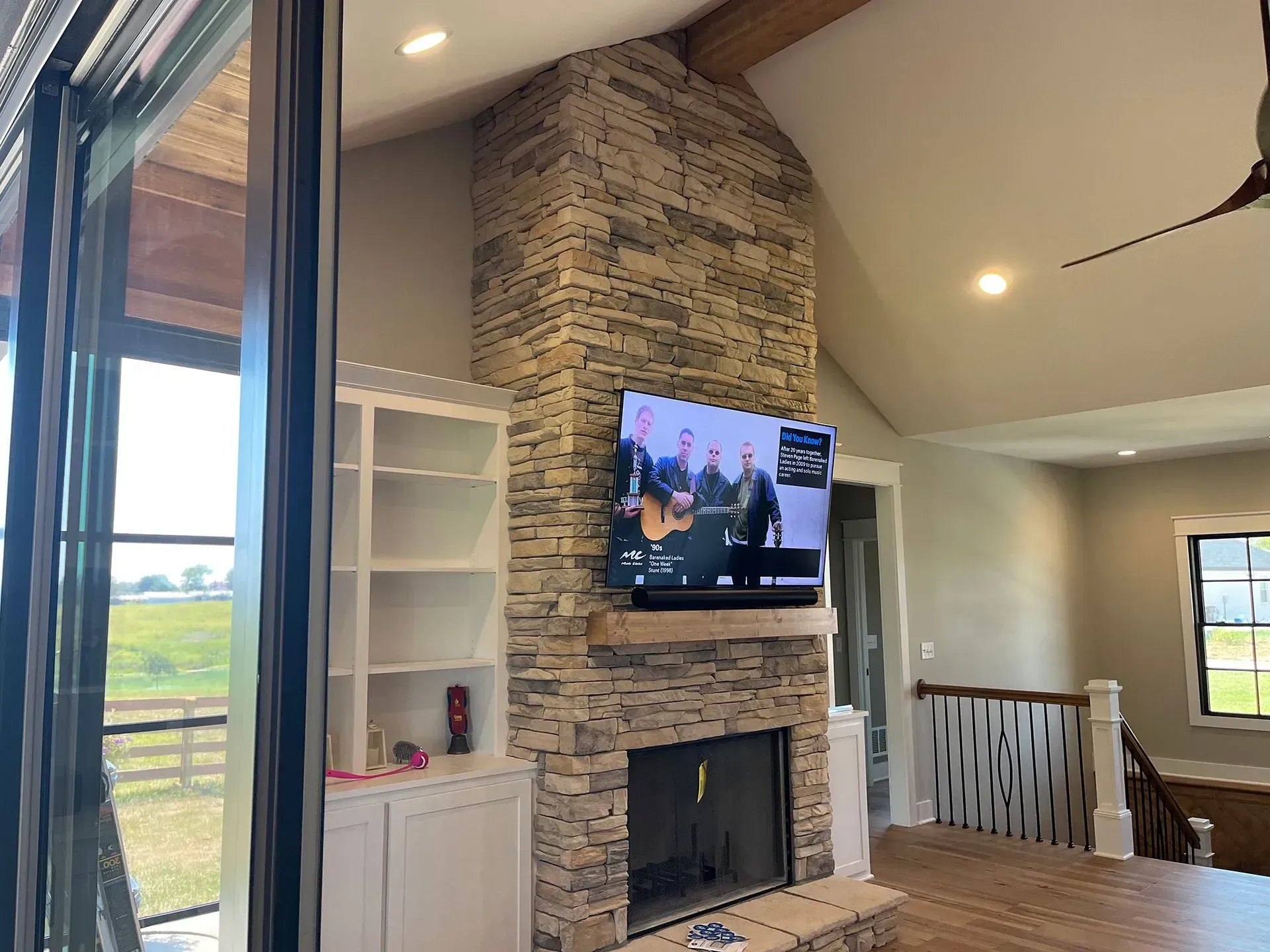 A stone fireplace with a mounted television and adjacent white shelving in a living room with vaulted ceilings.