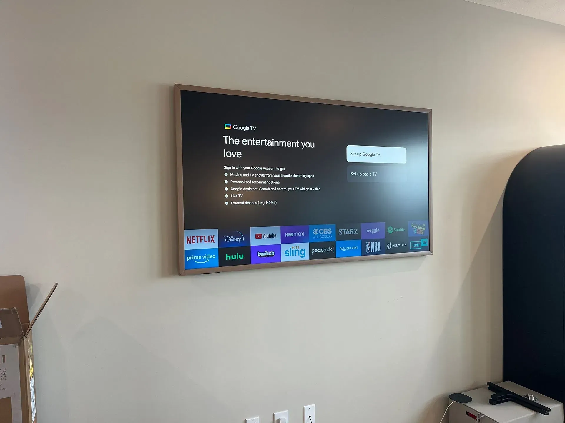 A wall-mounted smart TV displays a home screen menu with app icons in a sparsely furnished room.