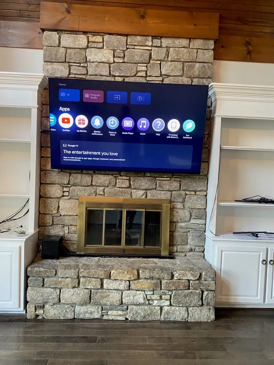 A stone fireplace with a mounted television and white built-in shelving on either side in a rustic-style room.