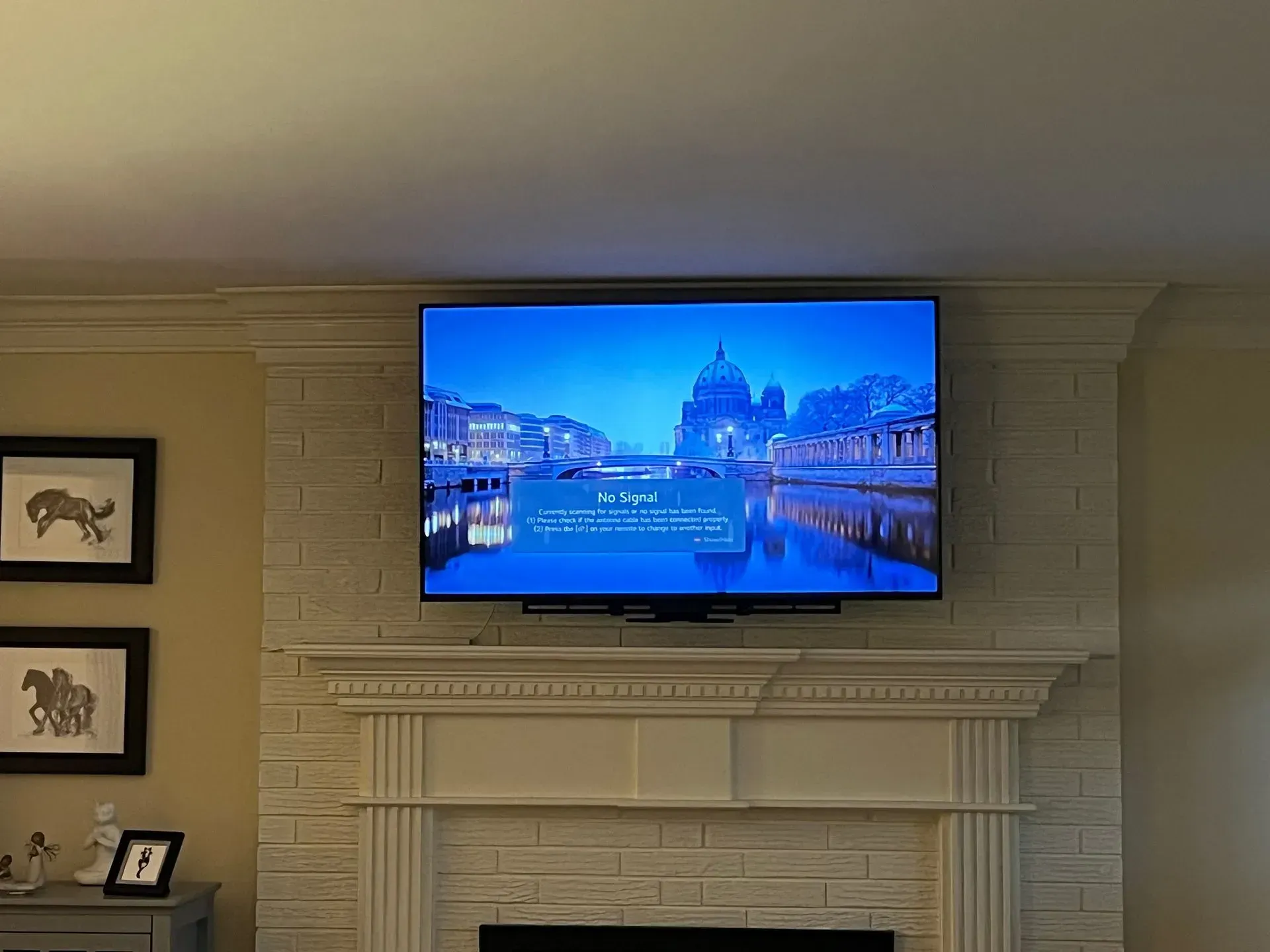 A flat-screen television mounted above a white brick fireplace shows a scenic blue water and bridge image with text.