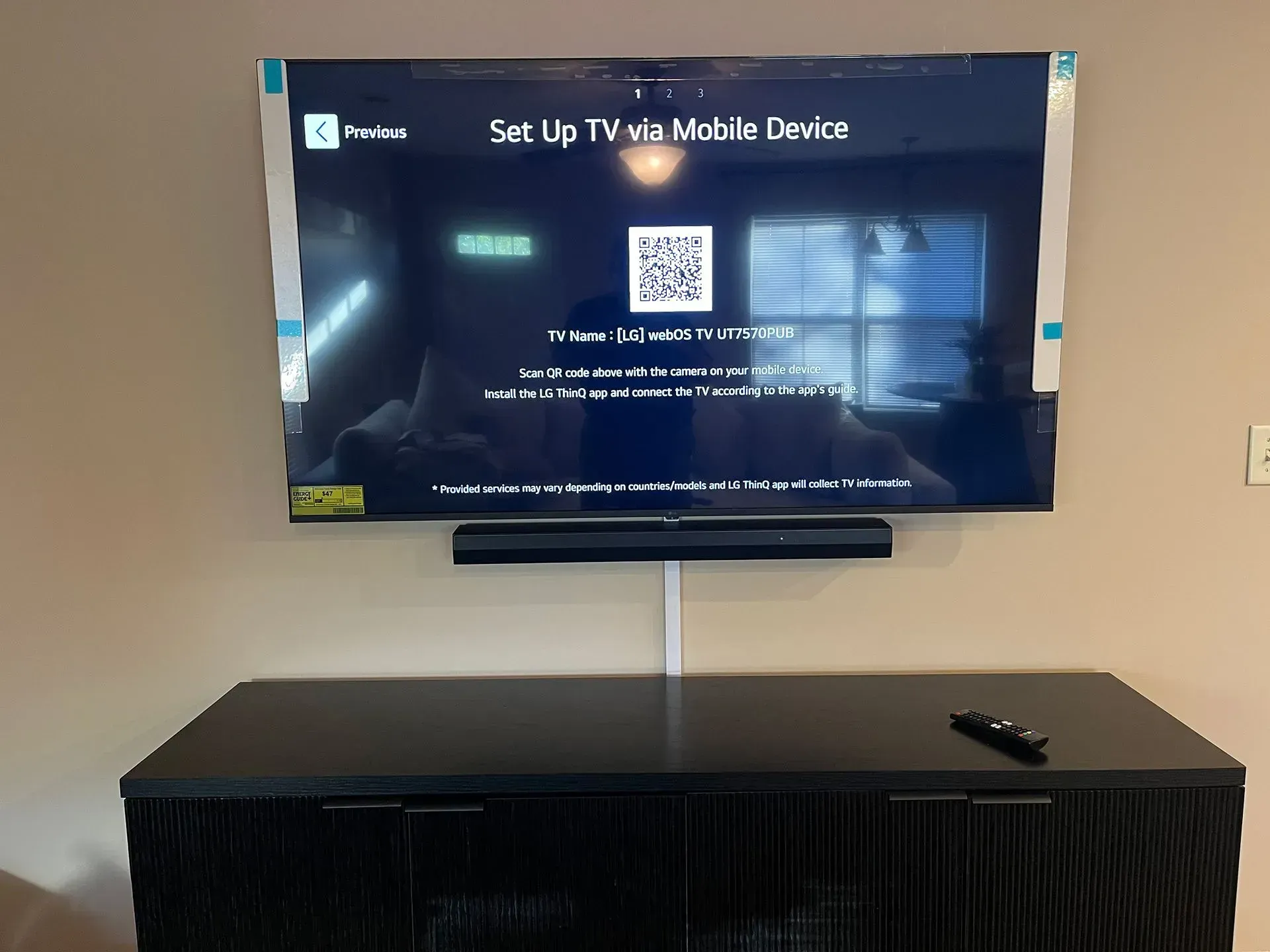 A wall-mounted TV displays a QR code for mobile setup, positioned above a dark console table in a room.