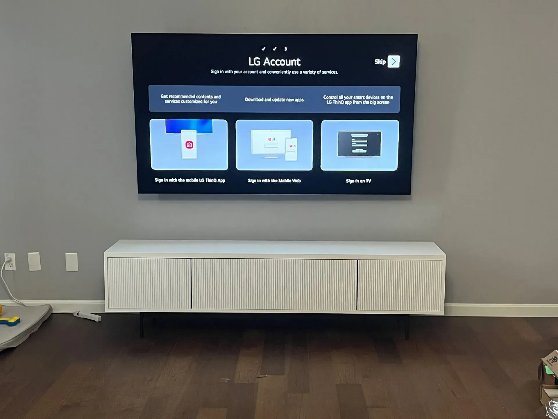 A flat-screen TV mounted on a light gray wall above a white, ribbed media console in a living room.