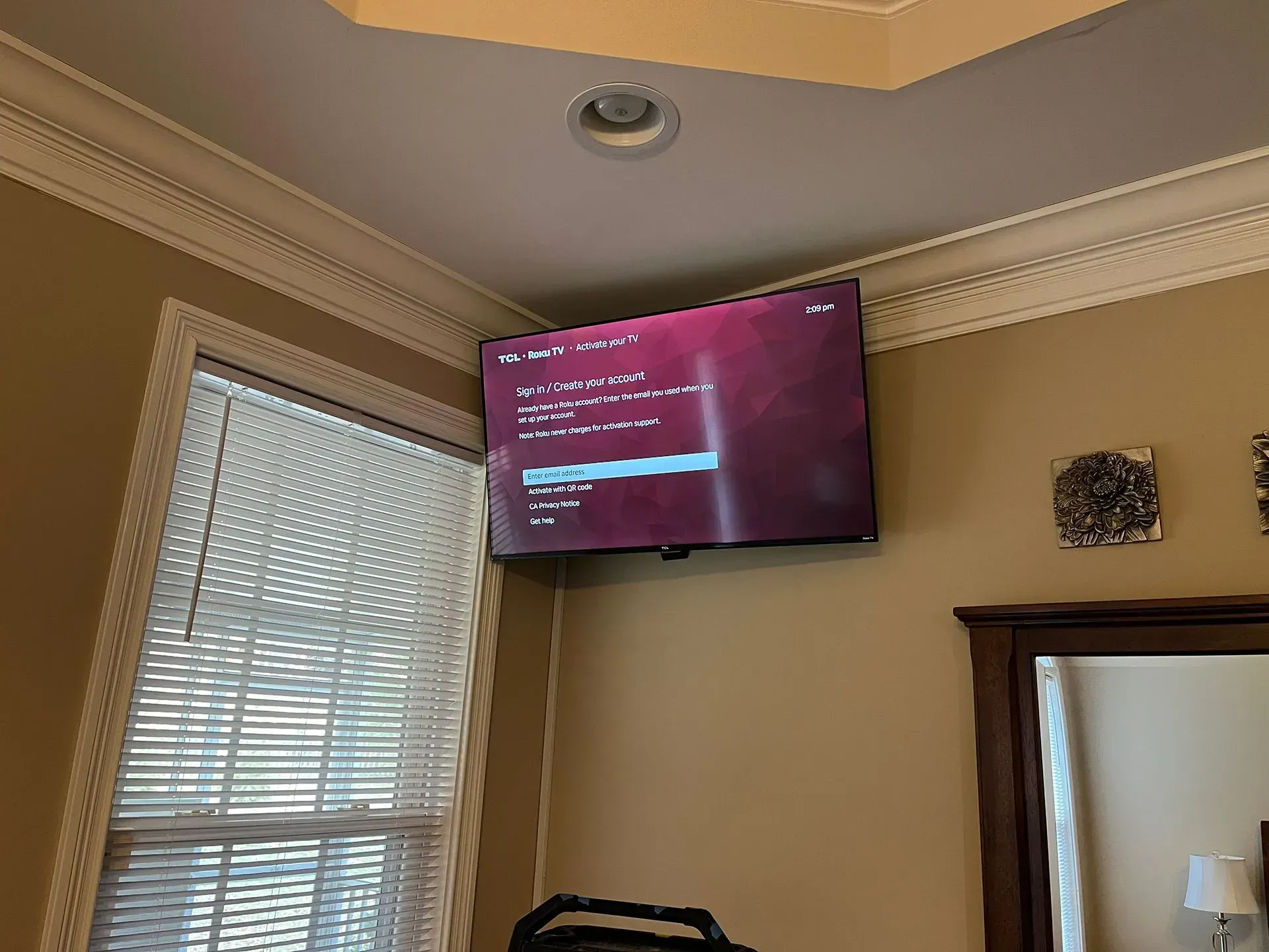 A television screen displaying a system error message, mounted high on a corner wall above a window with blinds.