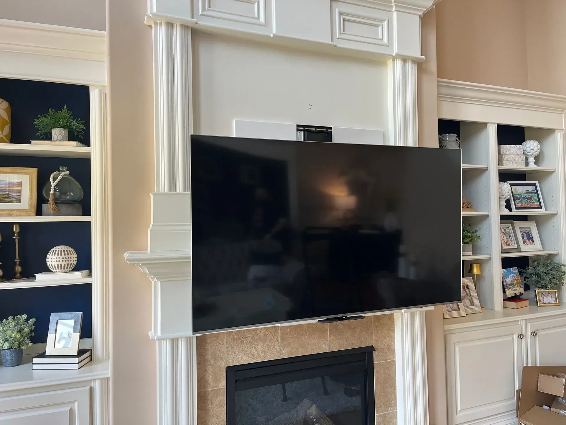 A wall-mounted television hangs above a fireplace, framed by built-in white shelves decorated with various home decor items.