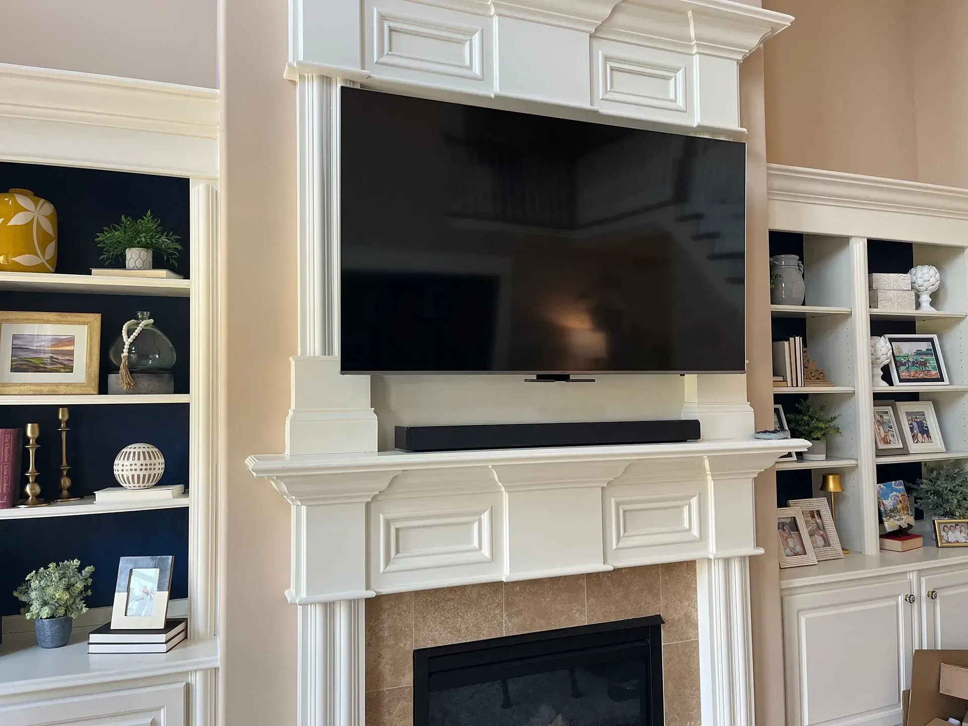 A white fireplace mantel with a mounted television and soundbar, flanked by built-in shelves filled with decor.