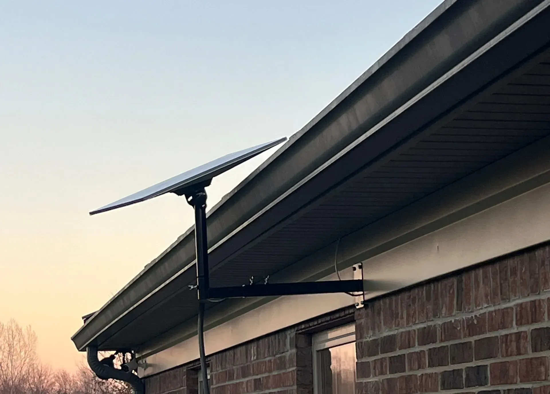 A Starlink satellite dish mounted on the exterior brick wall of a house under a clear, sunset sky.