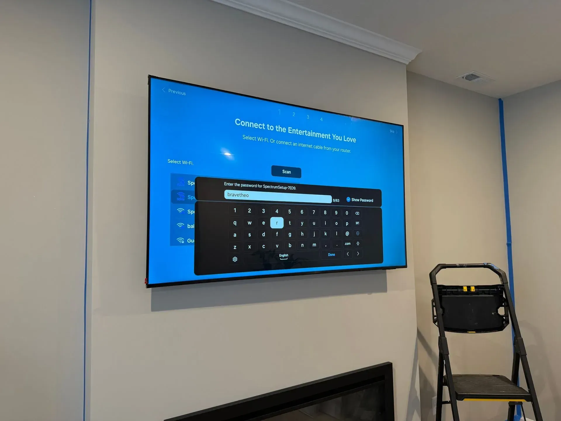 A mounted TV screen displays a Wi-Fi password prompt with an on-screen keyboard, positioned above a fireplace in a room.