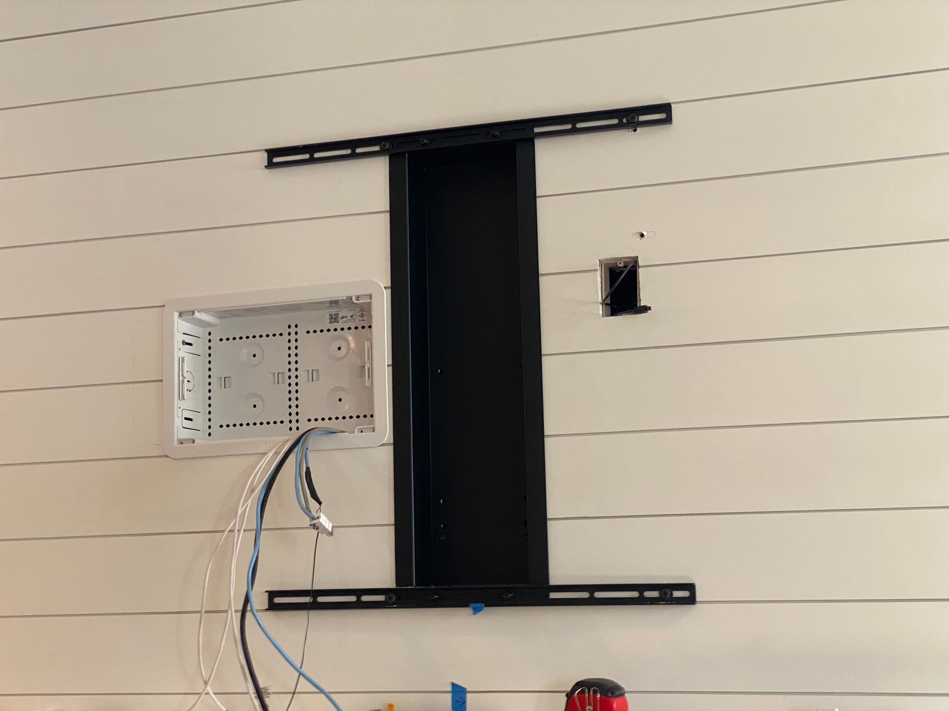 A white shiplap wall featuring a black recessed media box, a TV mounting bracket, and an open electrical junction box.