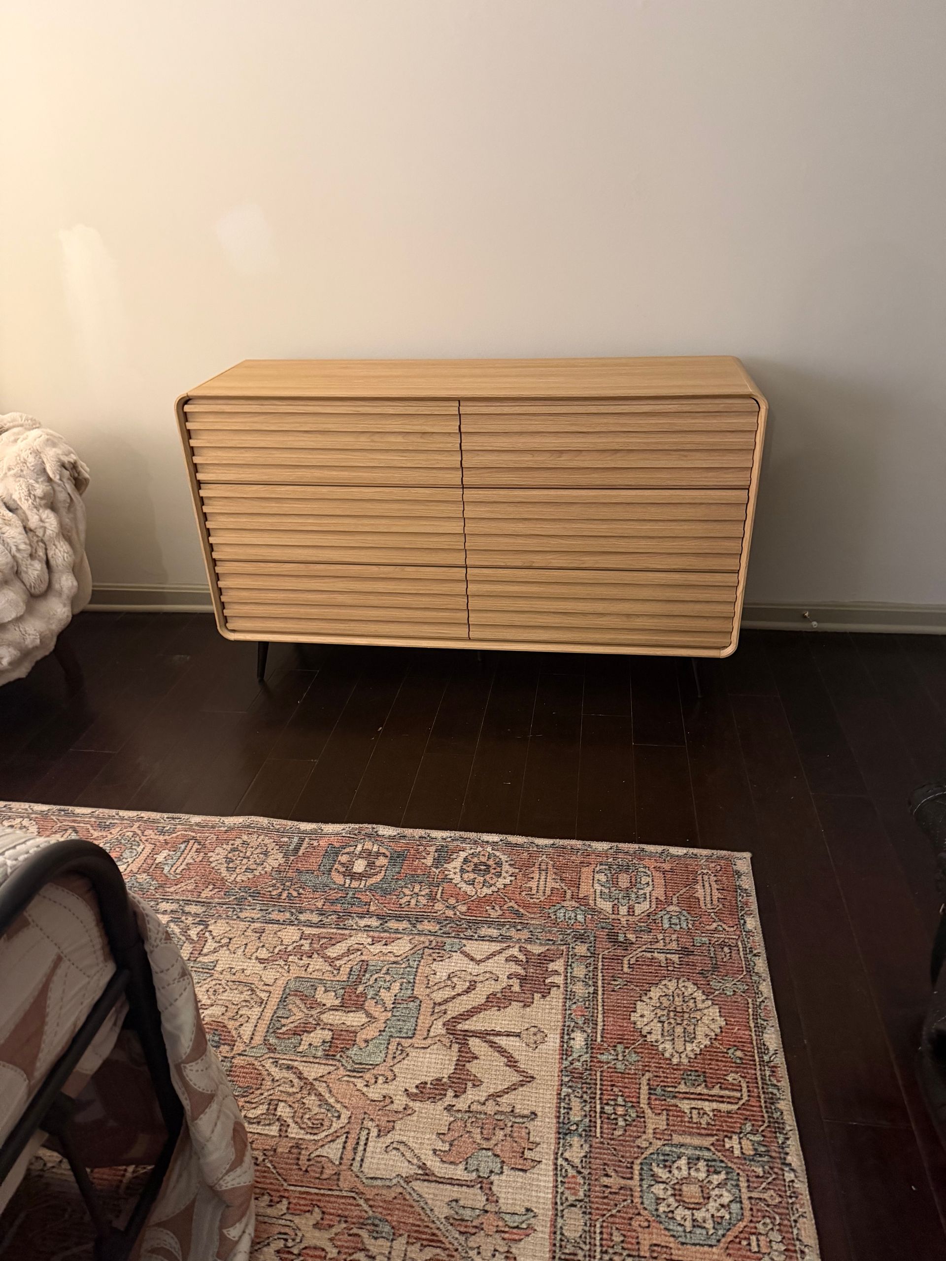 A light wood, mid-century modern style sideboard with a horizontal slatted texture, placed against a white wall.