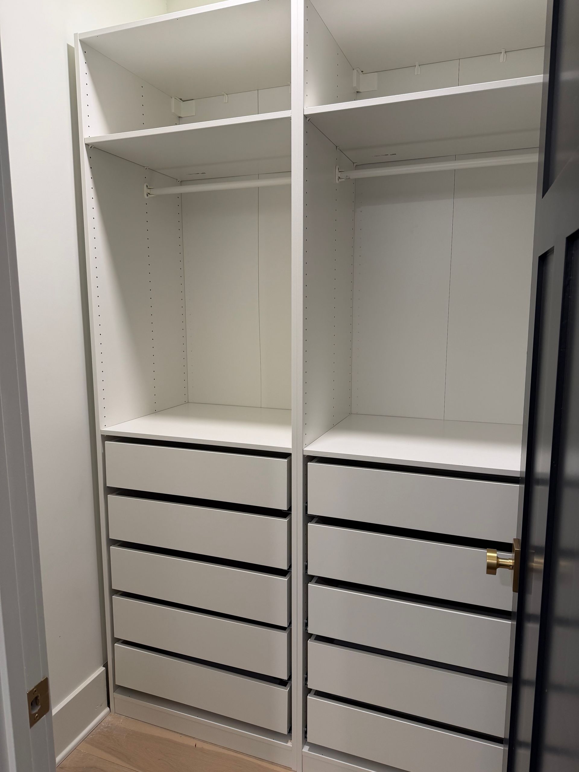 A walk-in closet featuring two vertical sections with white shelves, hanging rods, and sets of stacked drawers.