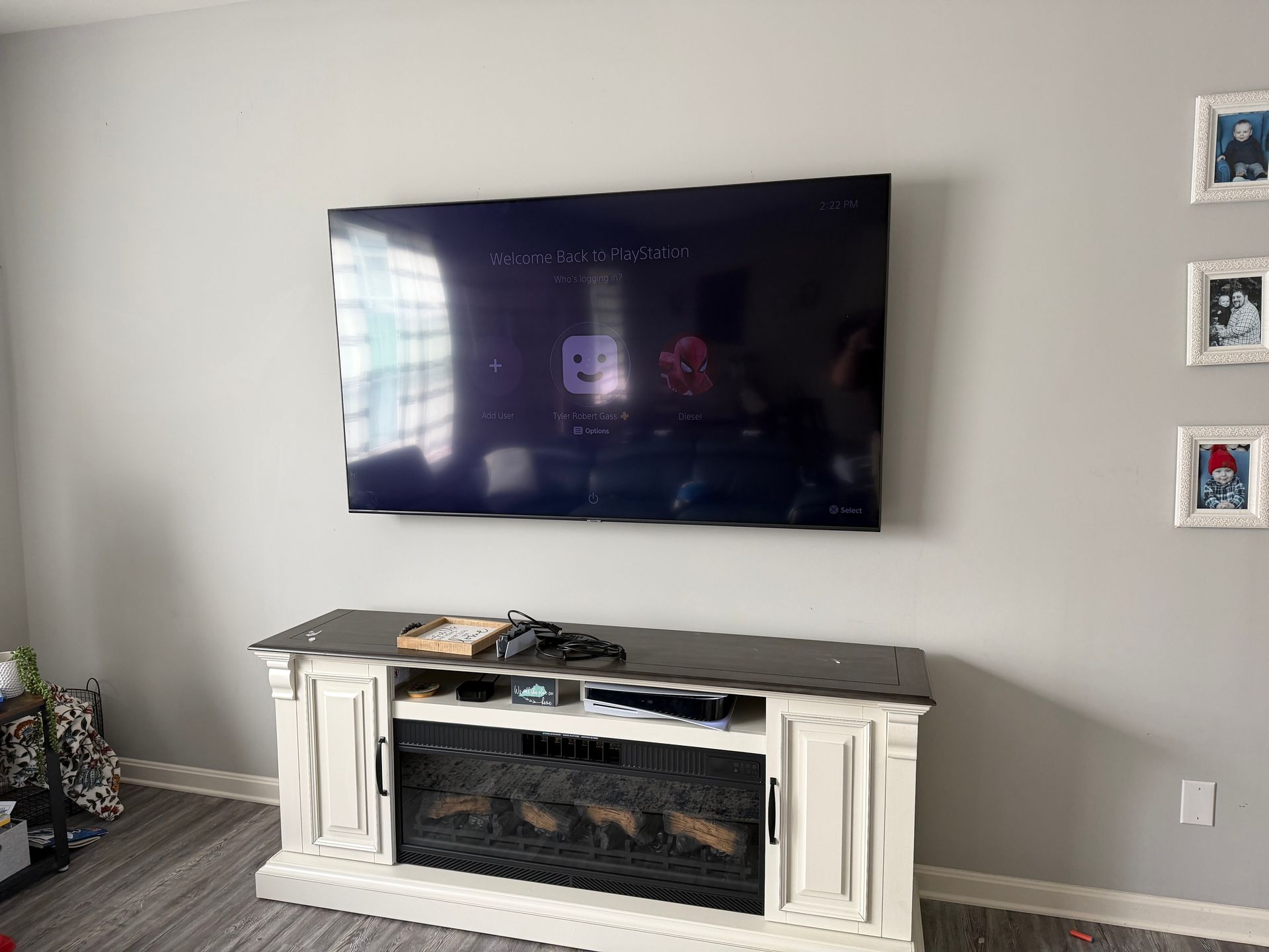 A large flat-screen TV mounted on a light gray wall above a white and dark wood electric fireplace media console.
