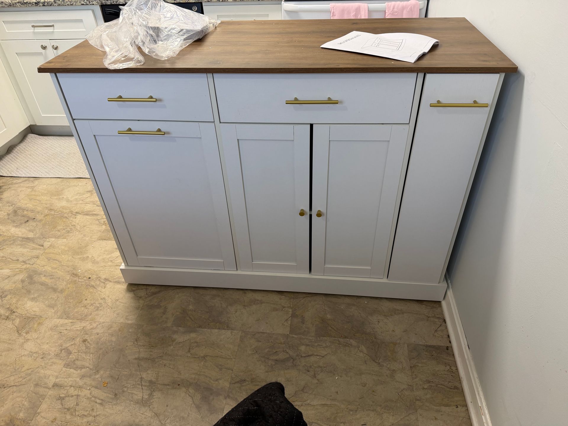 A light gray kitchen island with a dark wood top, gold handles, two drawers, two cabinet doors, and a side storage panel.