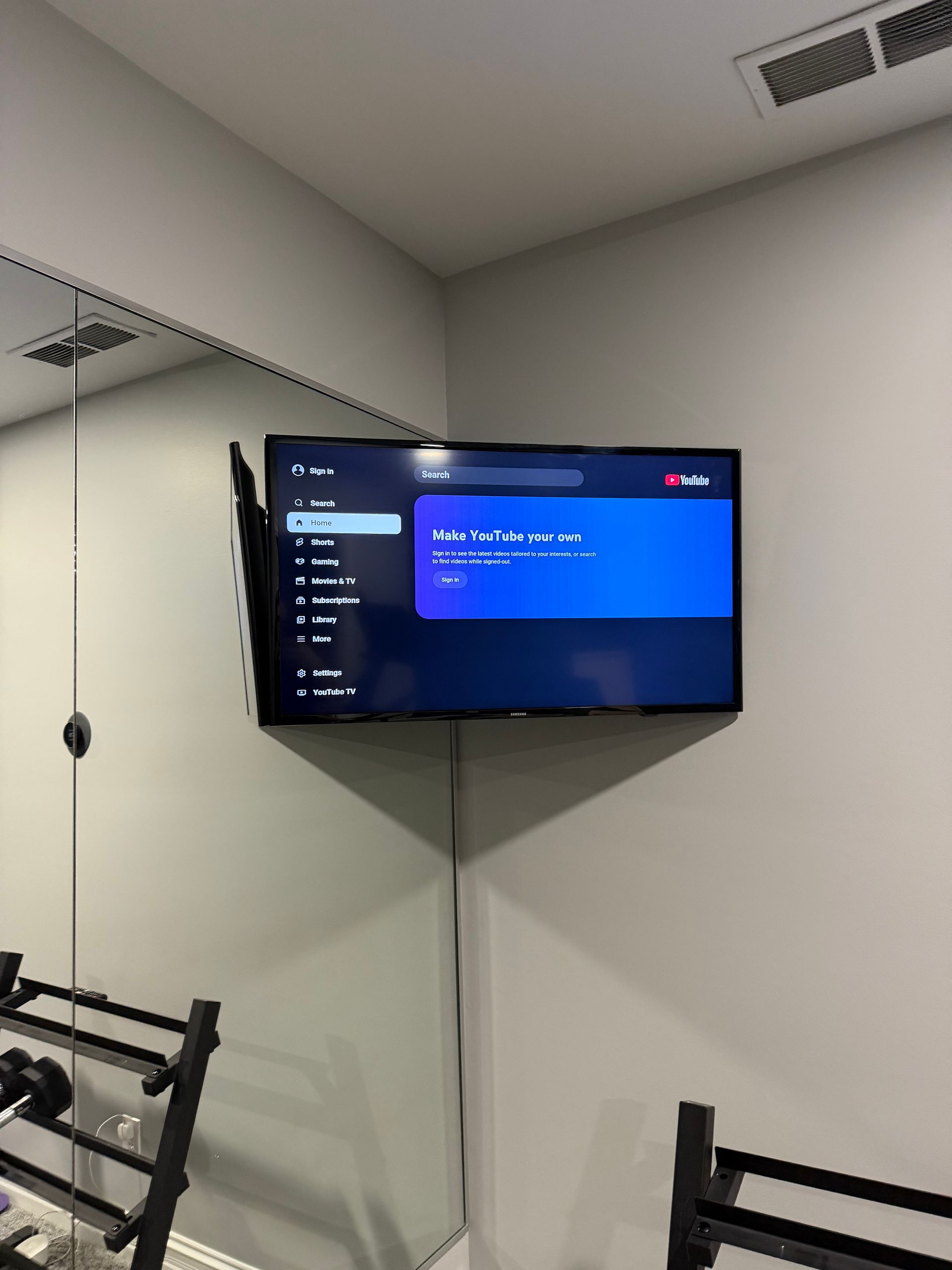 A television screen mounted on a wall in a home gym showing a menu interface with a blue highlights box.