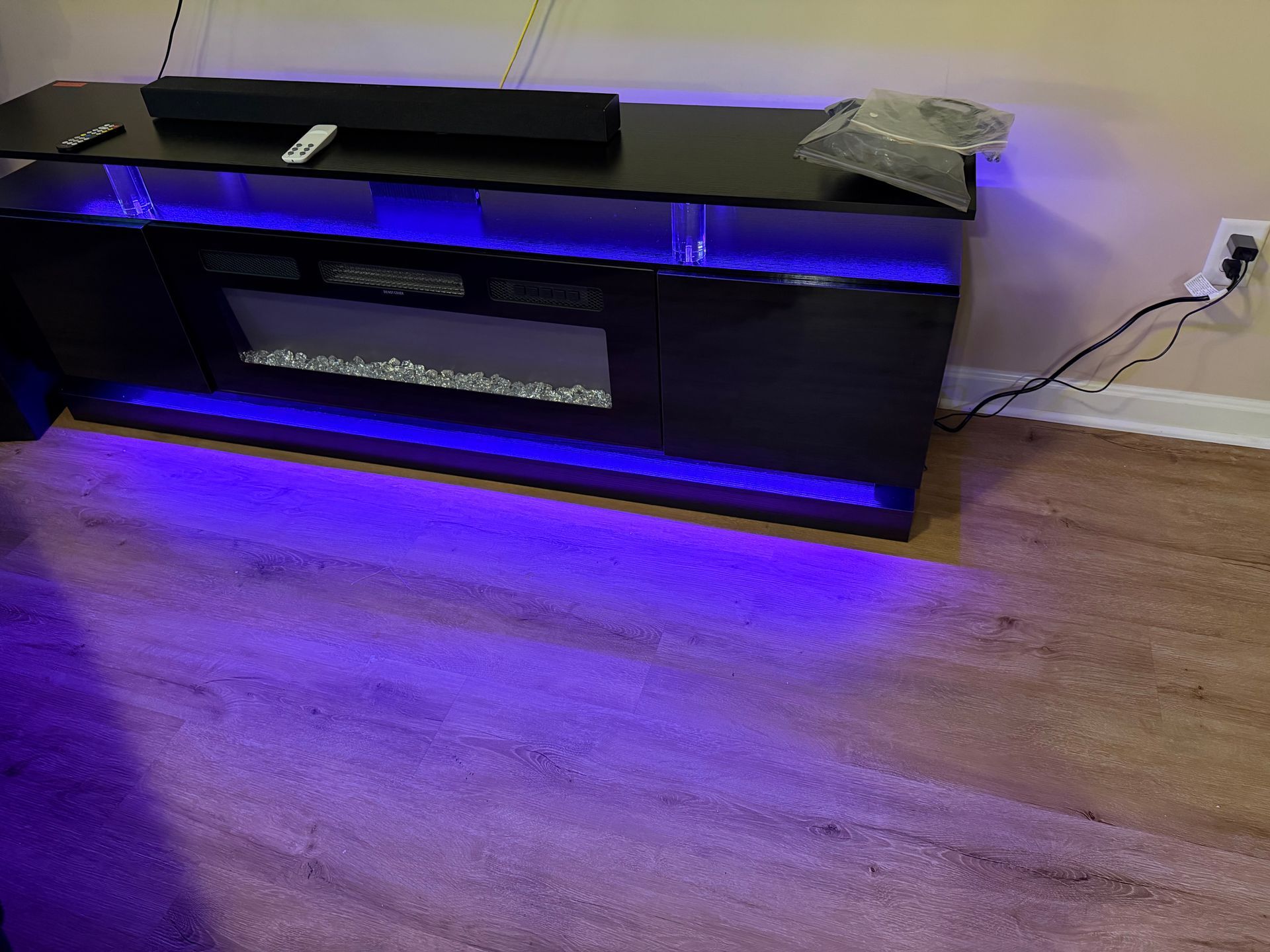 A black media console with an electric fireplace, illuminated by vibrant blue LED accent lighting on a wood floor.