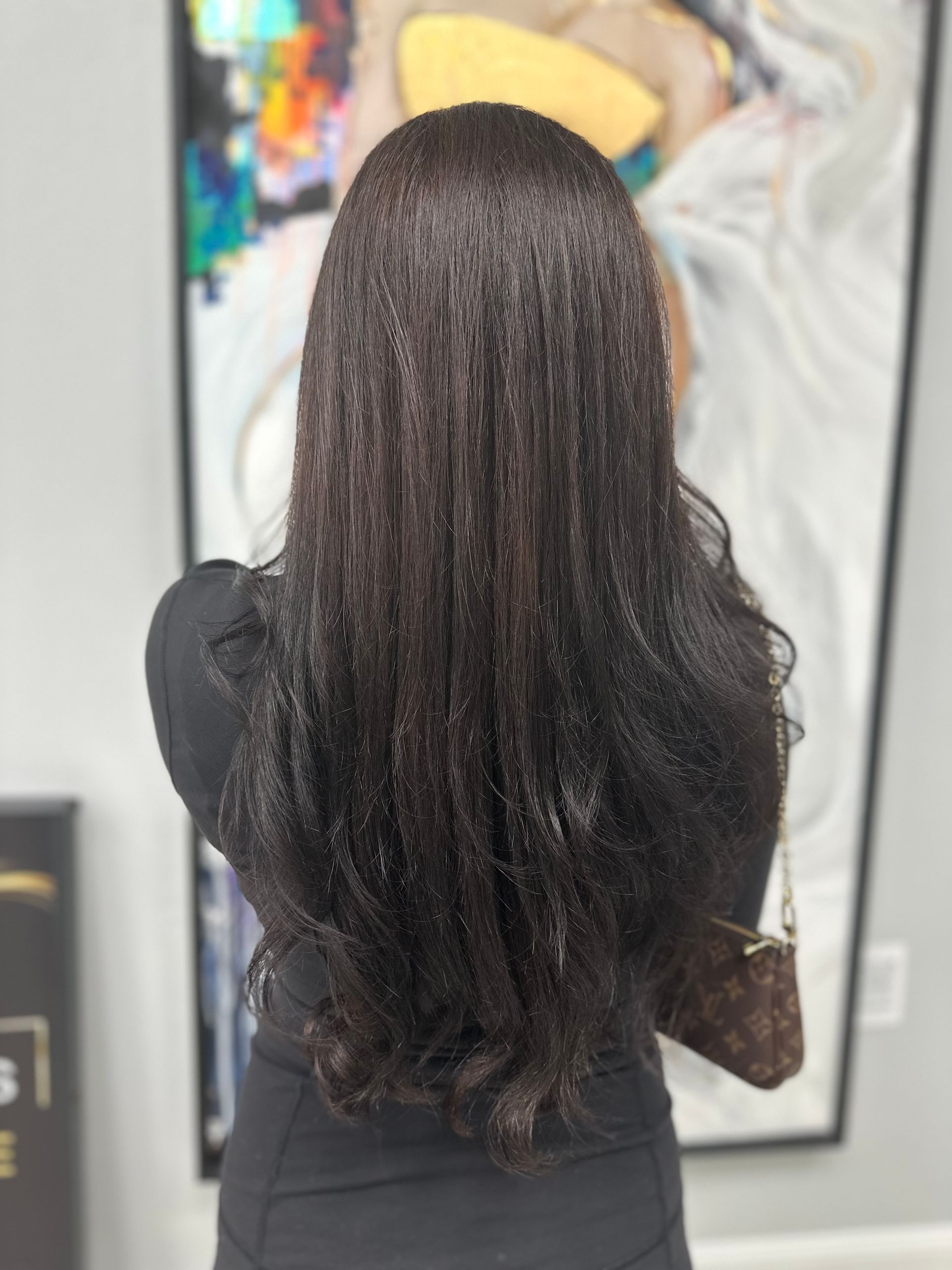 A woman with long black hair is standing in front of a painting.