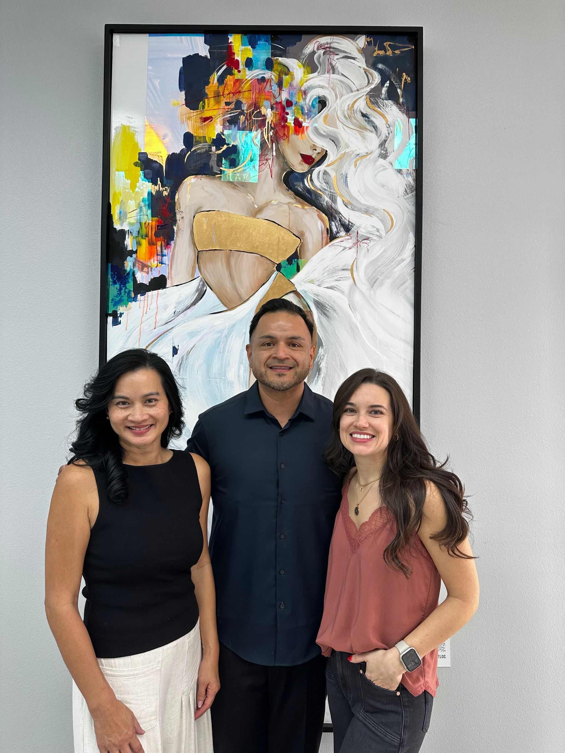 A man and two women are posing for a picture in front of a painting.