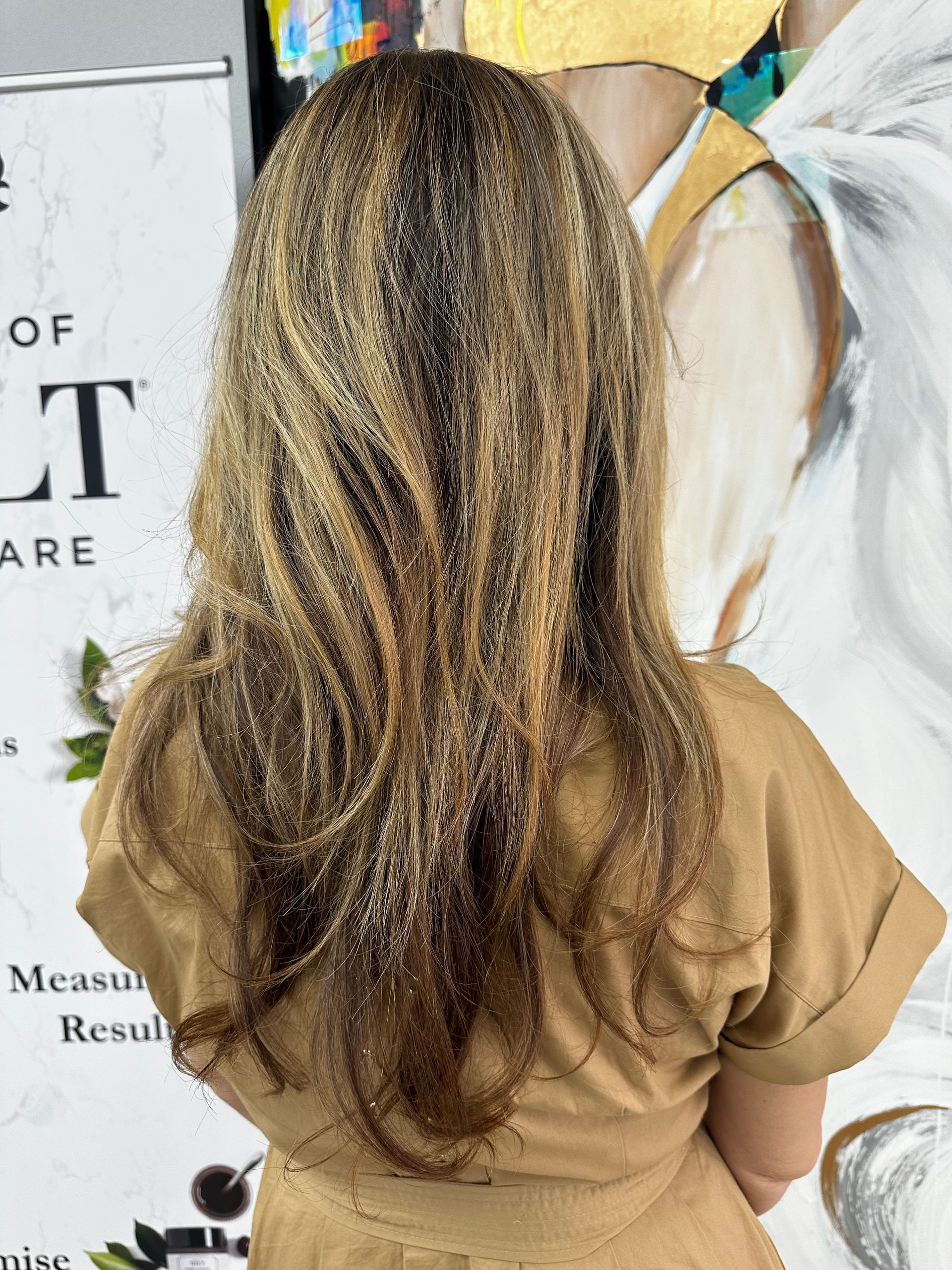 The back of a woman 's head with long hair and a tan dress.